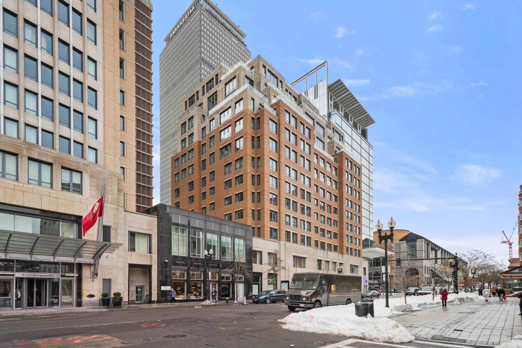 Urban condominium building with a brick facade and glass rooftop levels on a snowy downtown street.