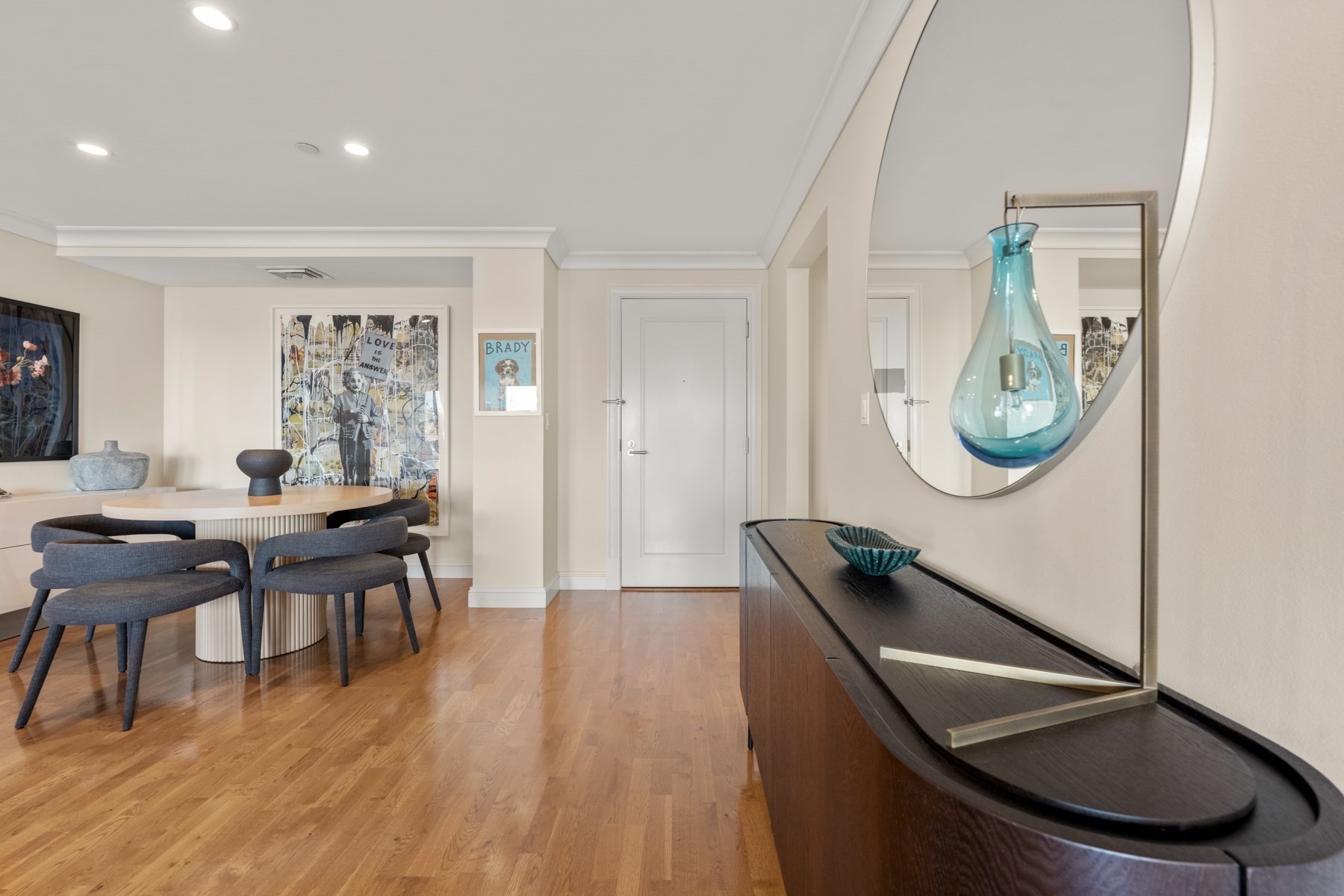 Furnished dining and entry area with a round table, gray chairs, hardwood floors, and a console beneath a mirror.
