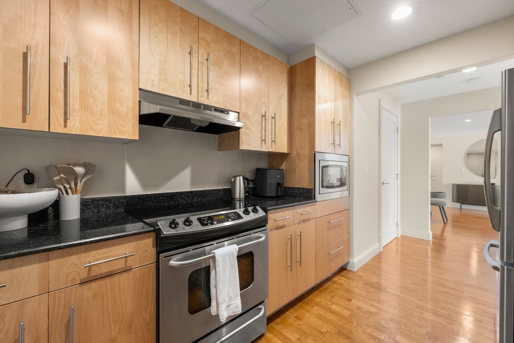 Modern kitchen with light wood cabinets, black countertops, and stainless-steel appliances.