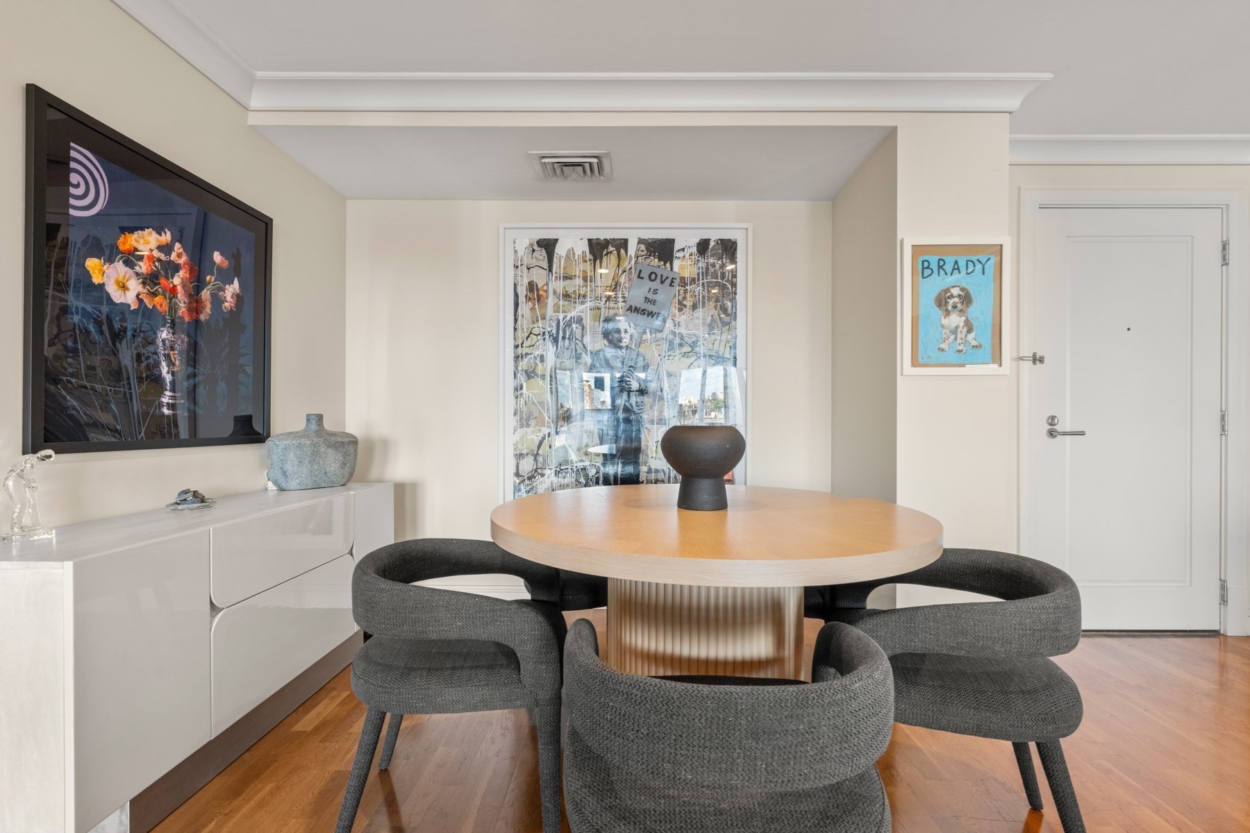 Dining room with a round wood table, charcoal chairs, hardwood floors, and prominent framed artwork.
