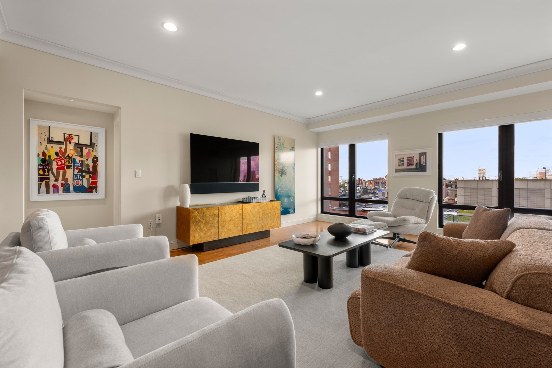 Living room with a wall-mounted television, sculptural cabinet, and large windows overlooking the city.