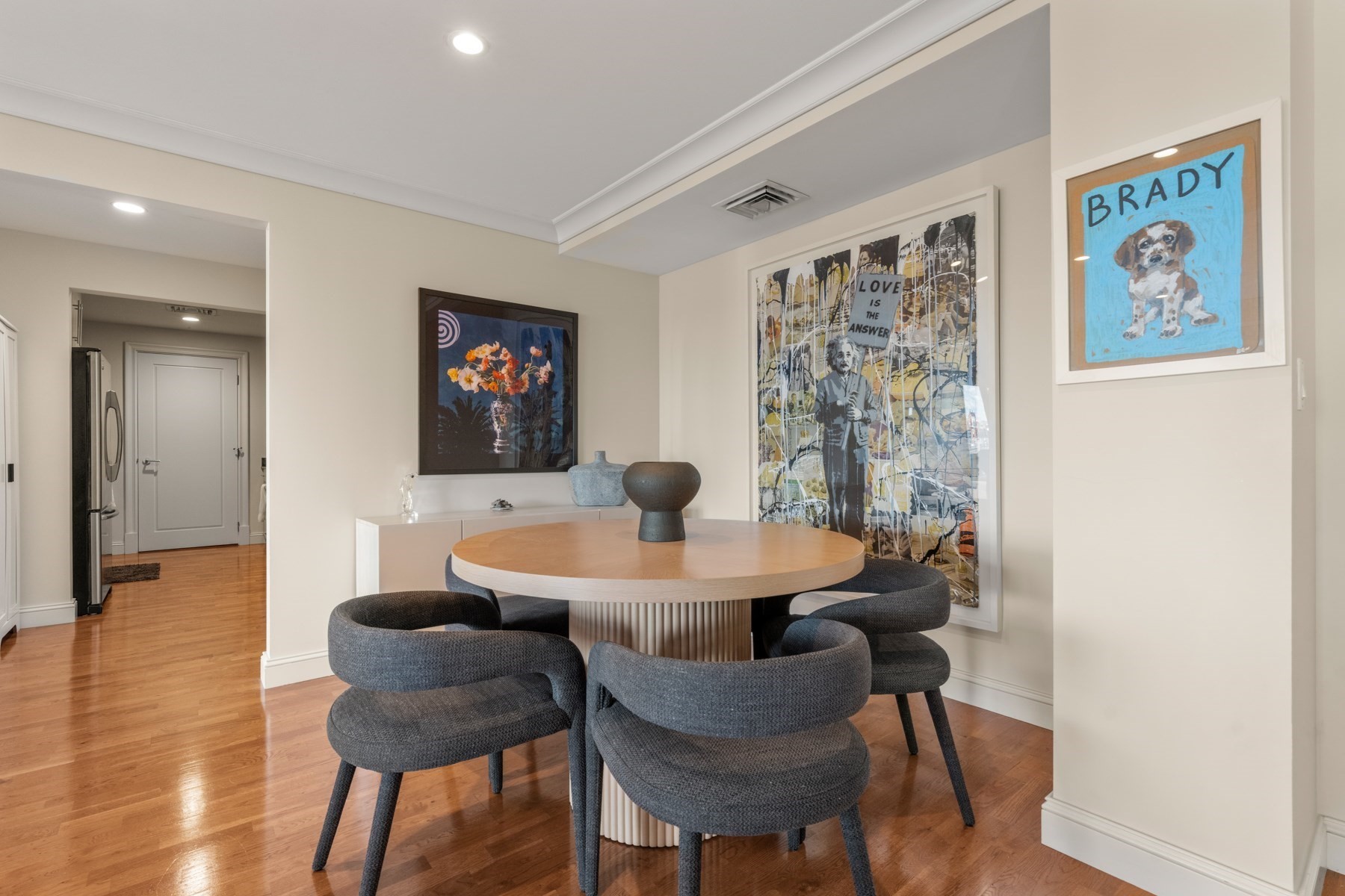 Dining area with a round wood table, charcoal chairs, hardwood floors, and large framed artwork.