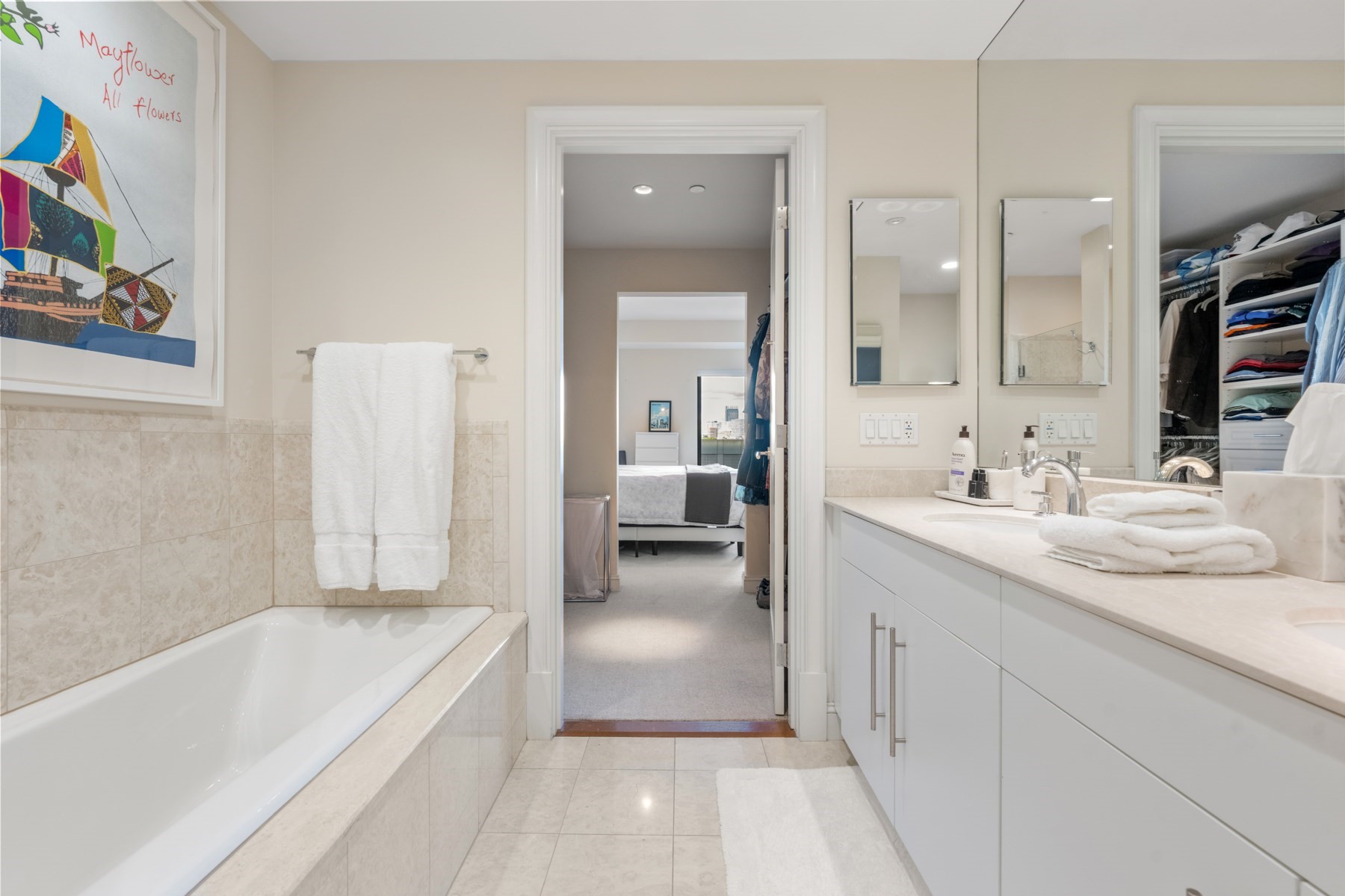 Bathroom with a tiled bathtub, double-mirror vanity, and doorway to a bedroom and closet.