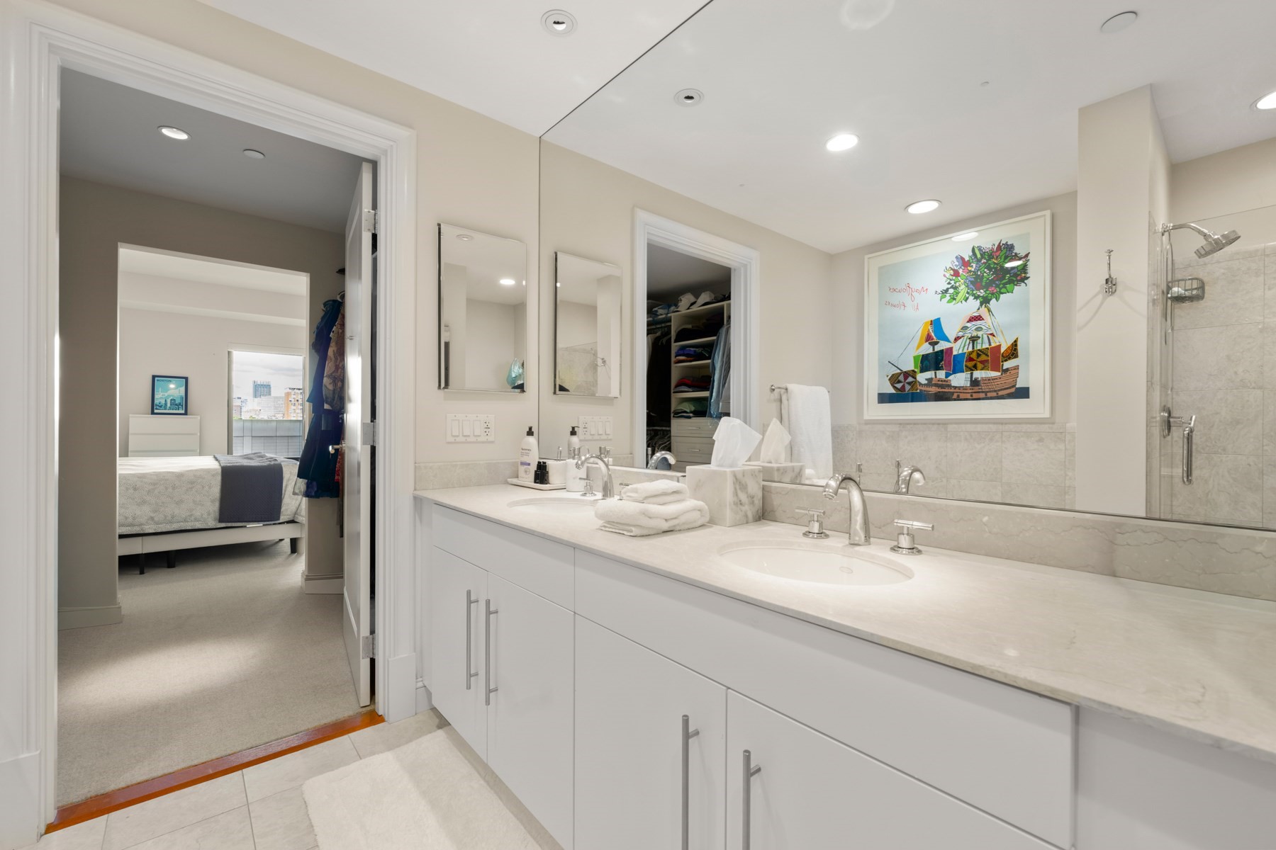 Primary bathroom with a long double vanity, mirrored wall, tiled glass shower, and doorway to the bedroom.