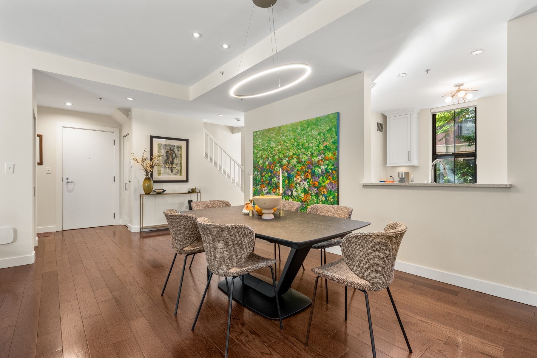 Condo dining area with woven chairs, hardwood floors, large floral artwork, and a kitchen pass-through.