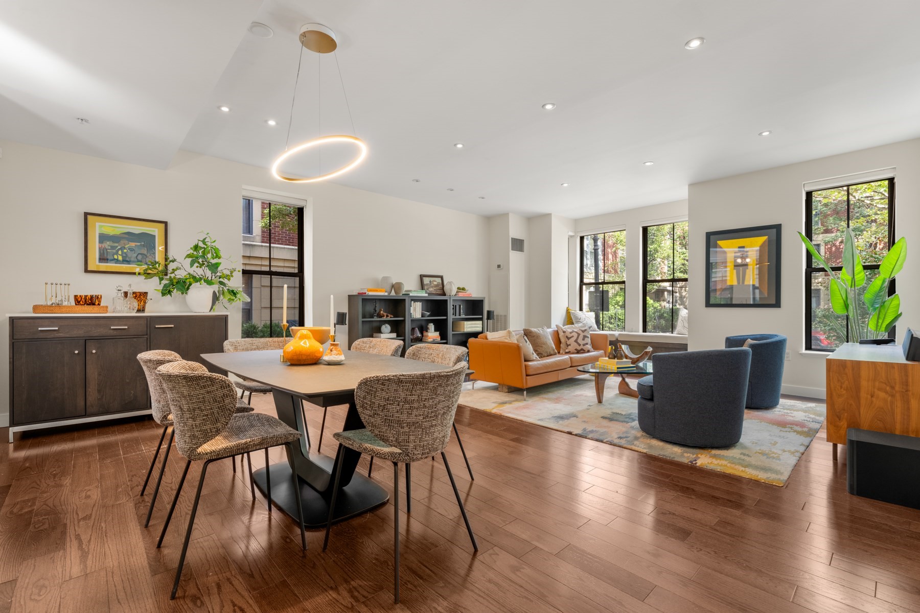 Open-plan living and dining room with hardwood floors, large windows, and a ring pendant light.
