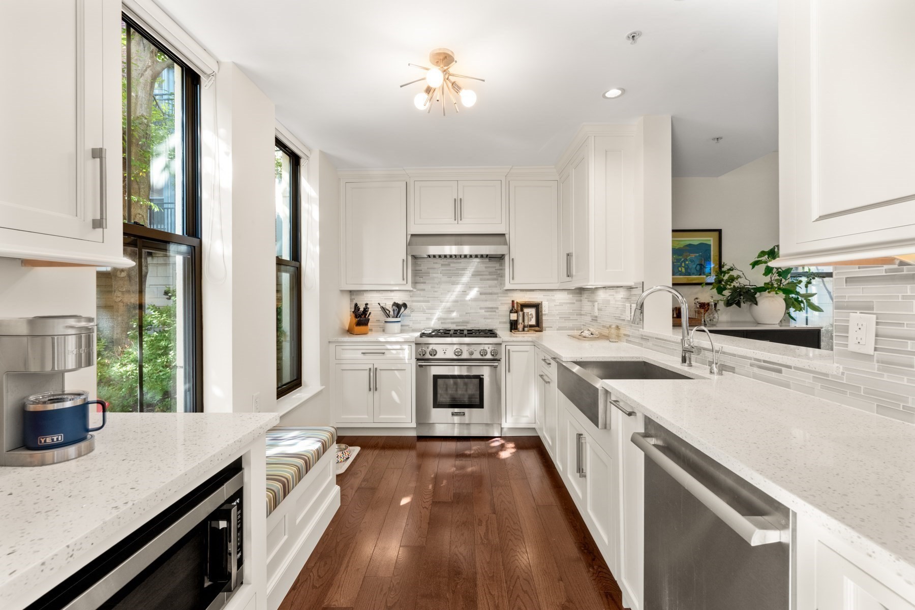 Bright white kitchen with a farmhouse sink, stainless-steel range, tall windows, and dark wood floors.