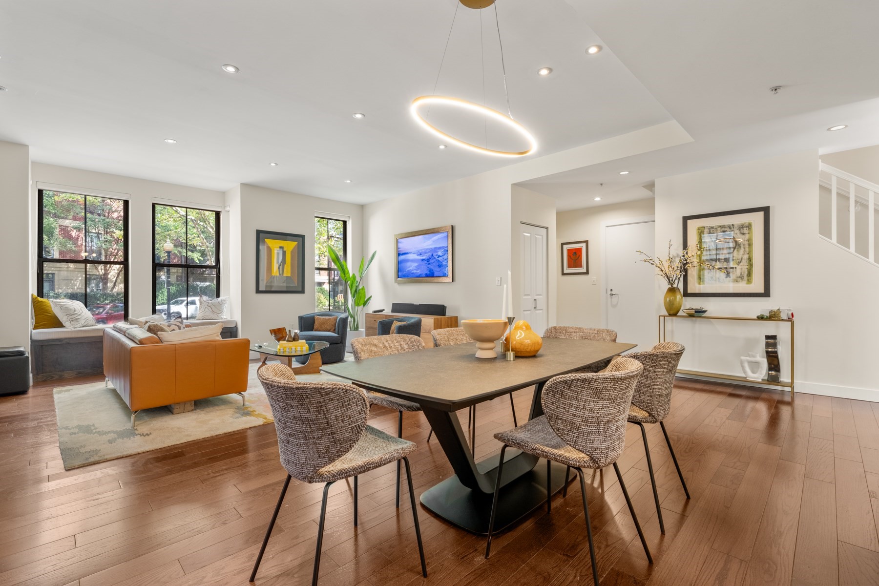 Open-plan living and dining room with large windows, an orange sofa, and woven dining chairs.