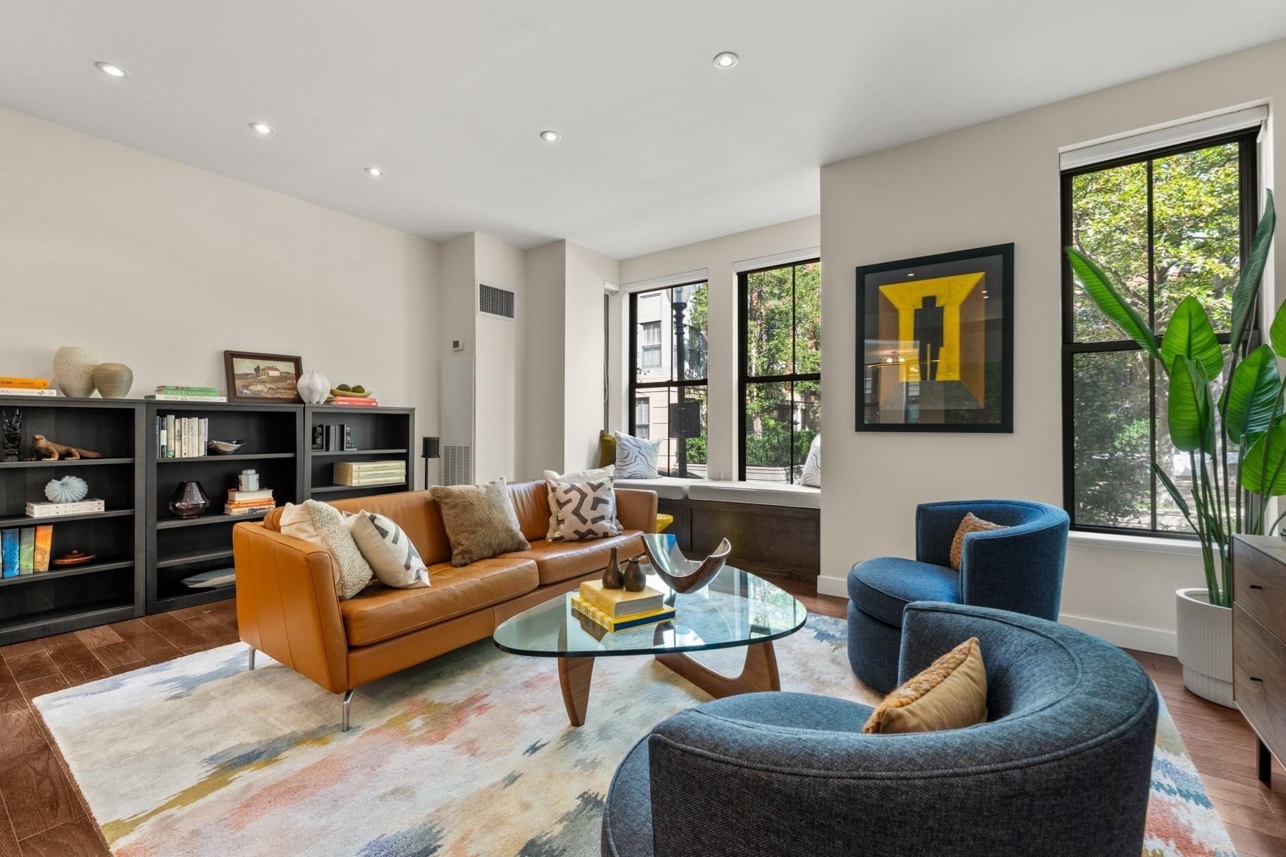 Living room with a caramel leather sofa, curved blue chairs, and large windows.