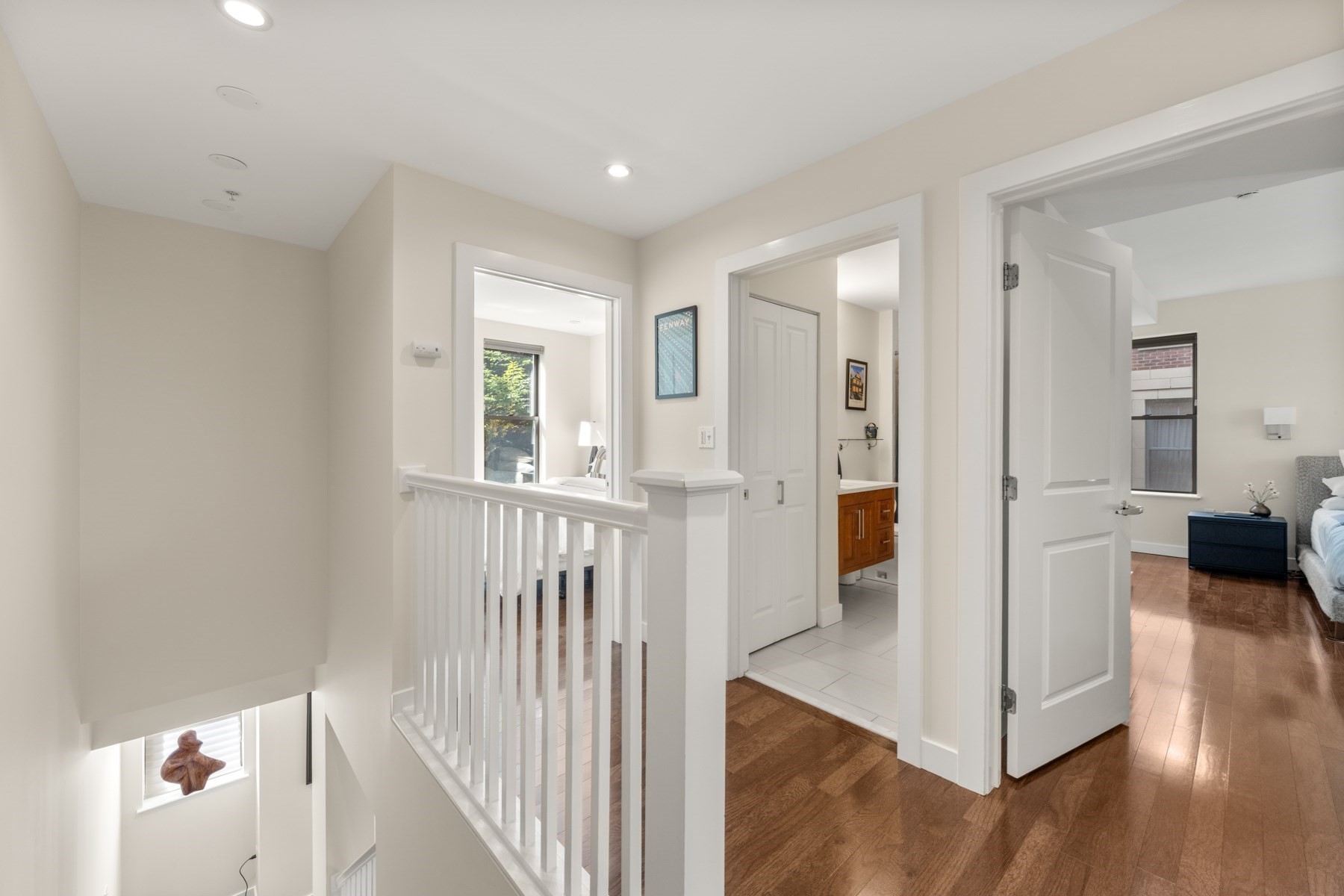 Upstairs hallway with white stair railing, hardwood floors, and open bathroom and bedroom doors.
