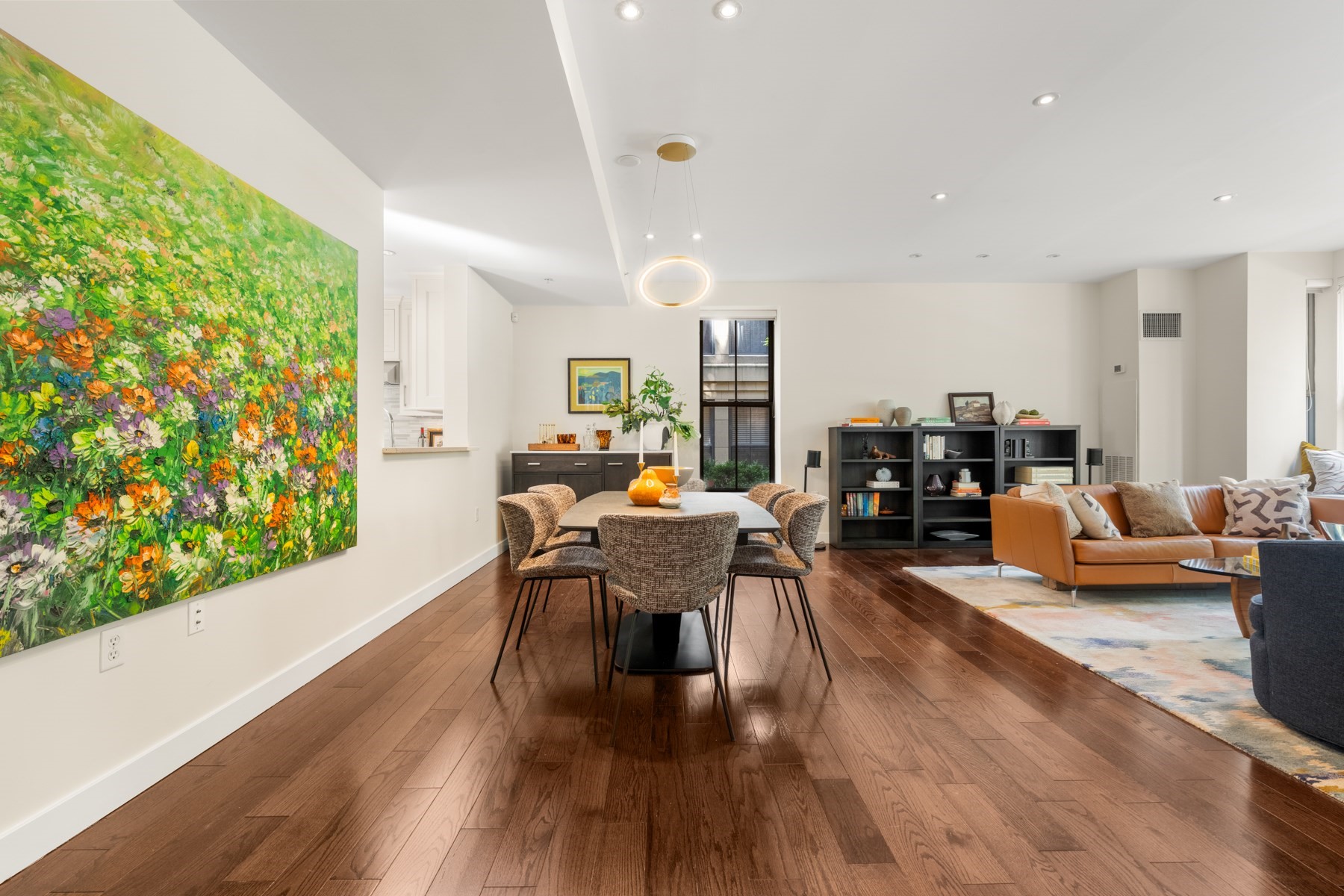 Open-plan living and dining room with hardwood floors, colorful artwork, and a tan leather sofa.