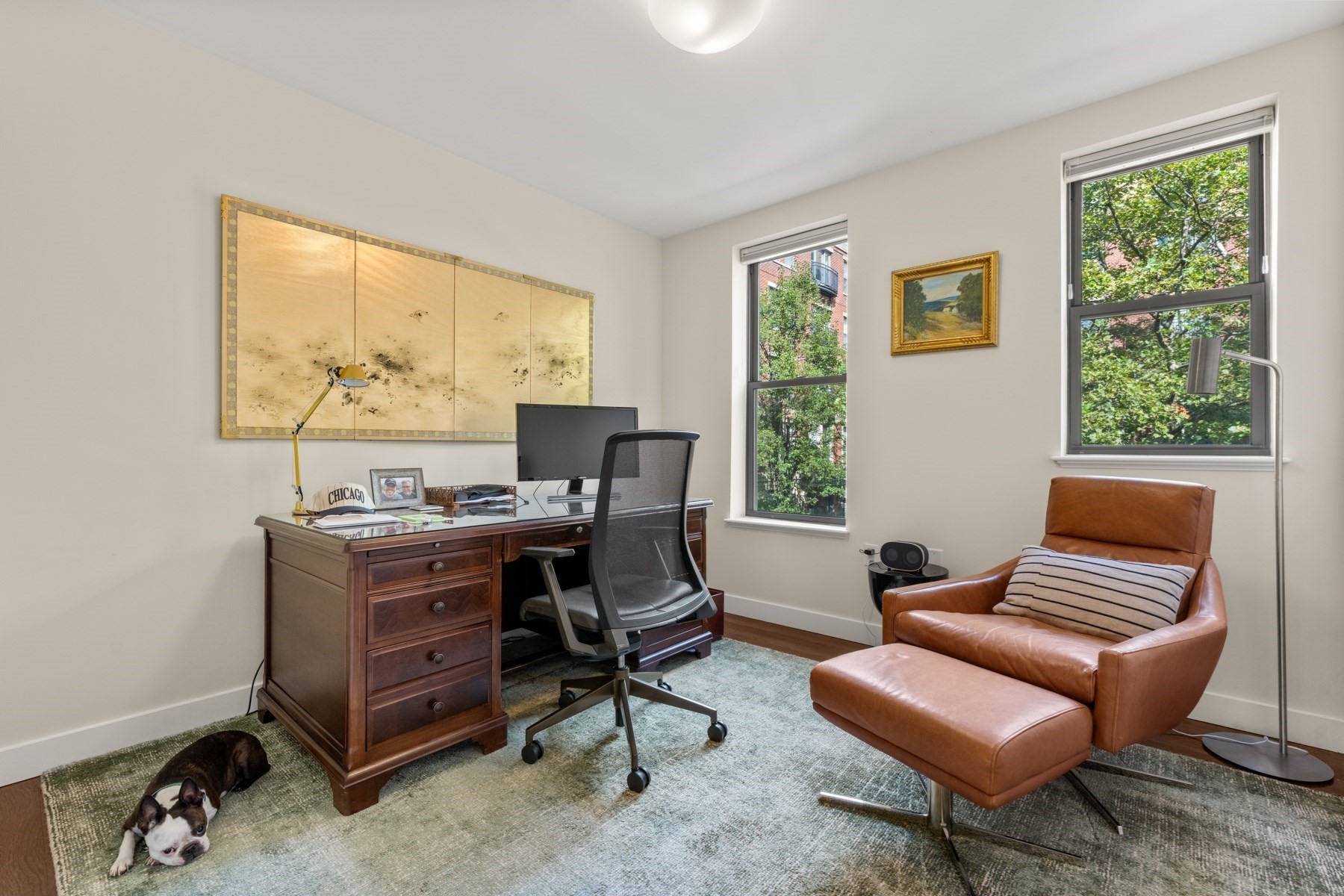 Home office with a dark wood desk, leather armchair, and small dog on the rug.
