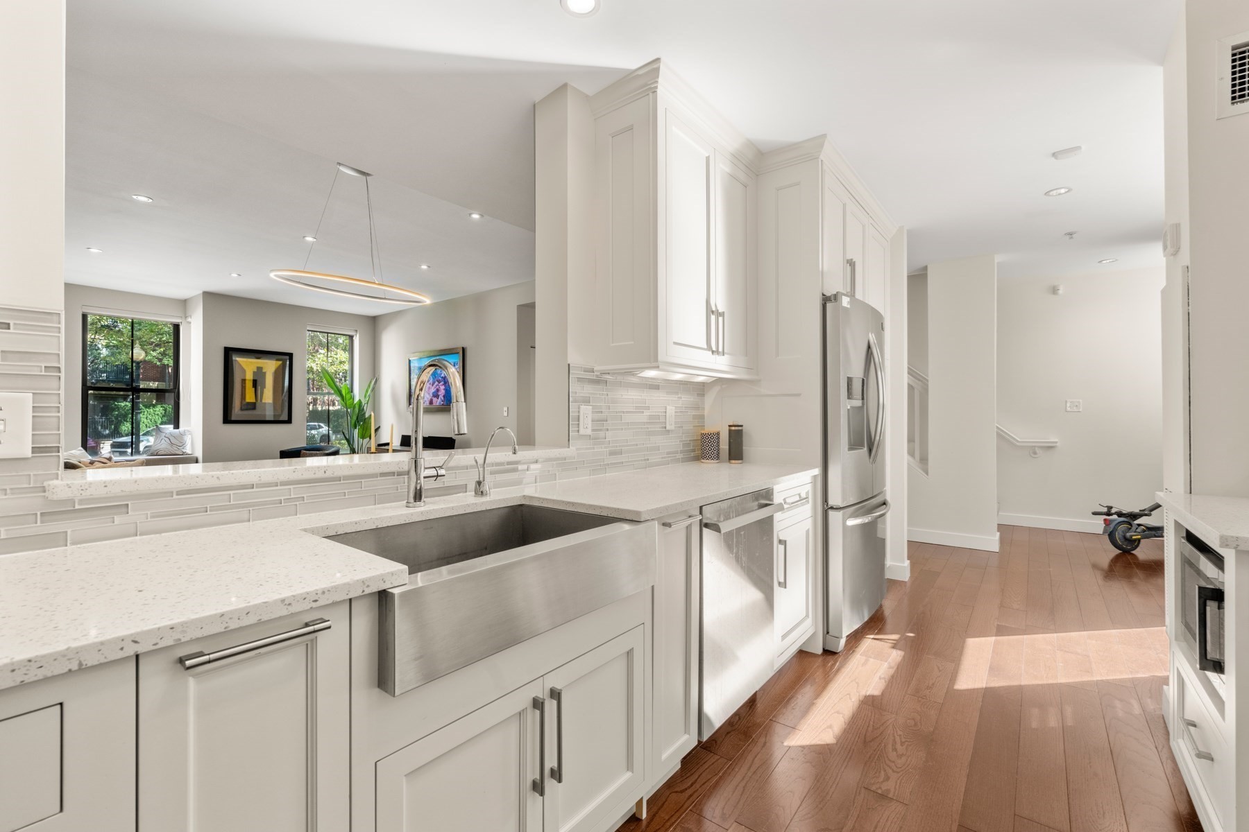 Modern kitchen with white cabinetry, a stainless farmhouse sink, quartz counters, and hardwood floors.