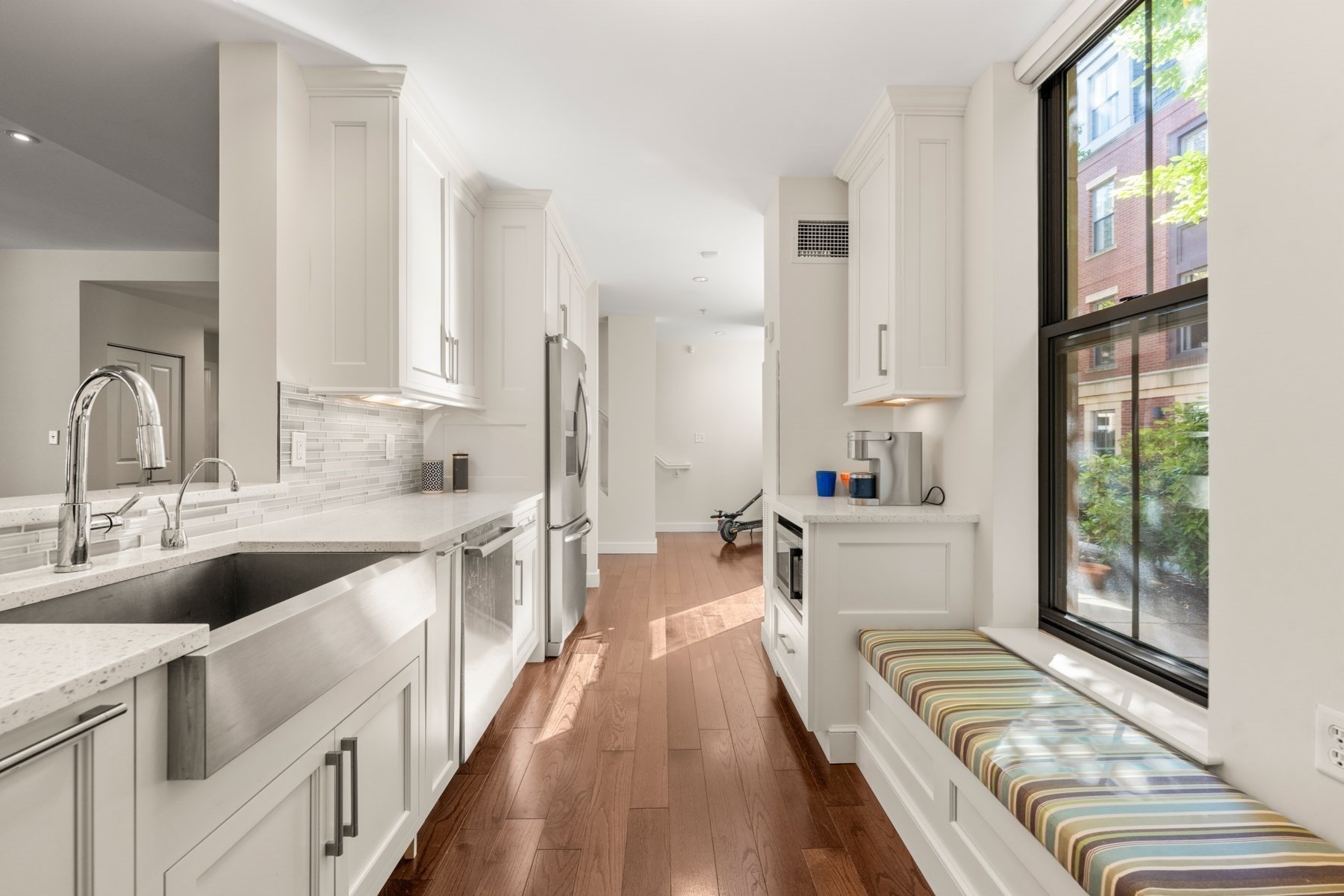 Bright white kitchen with a large stainless sink, wood floors, and a striped window seat.