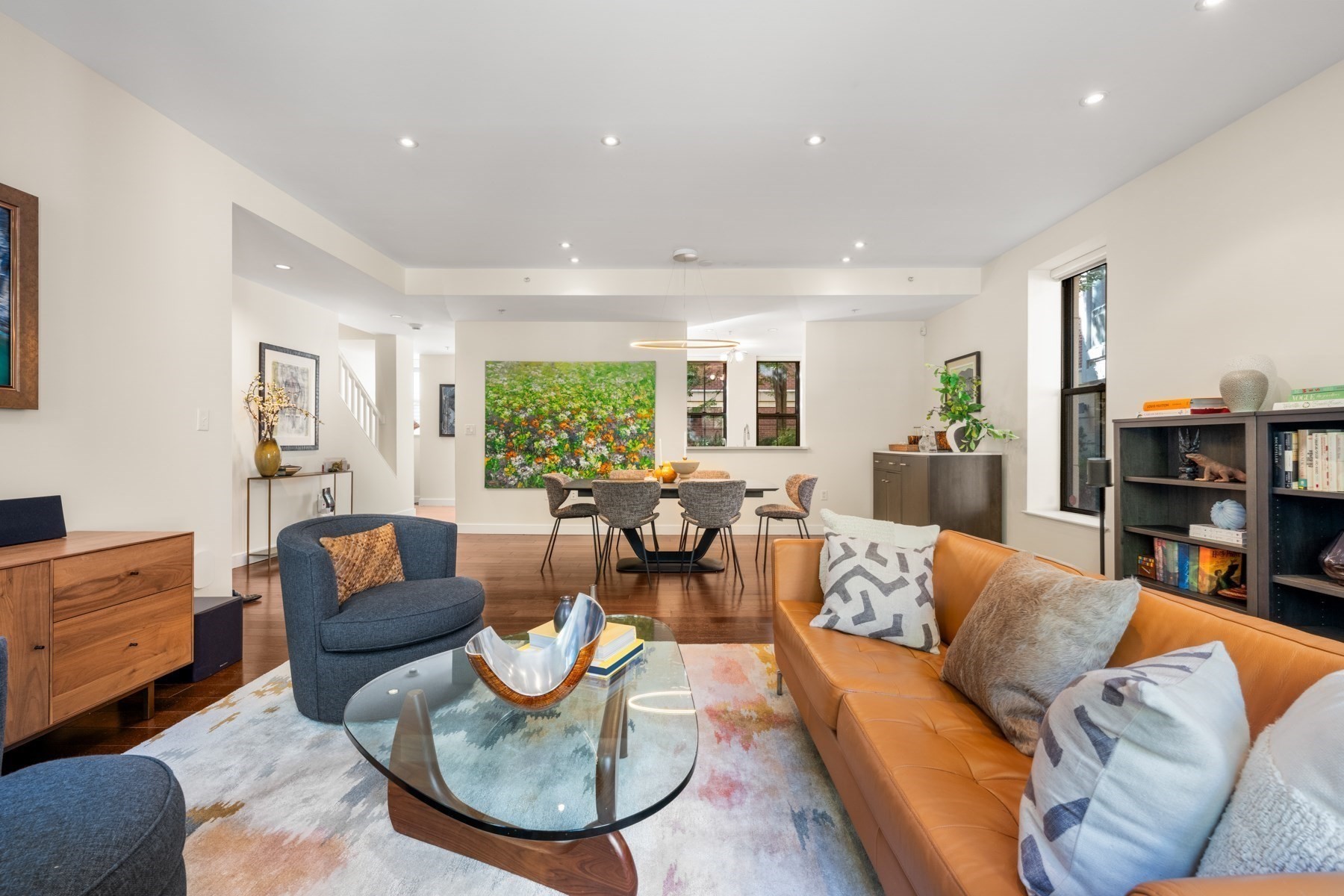 Open-plan living and dining room with a tan leather sofa and colorful artwork.