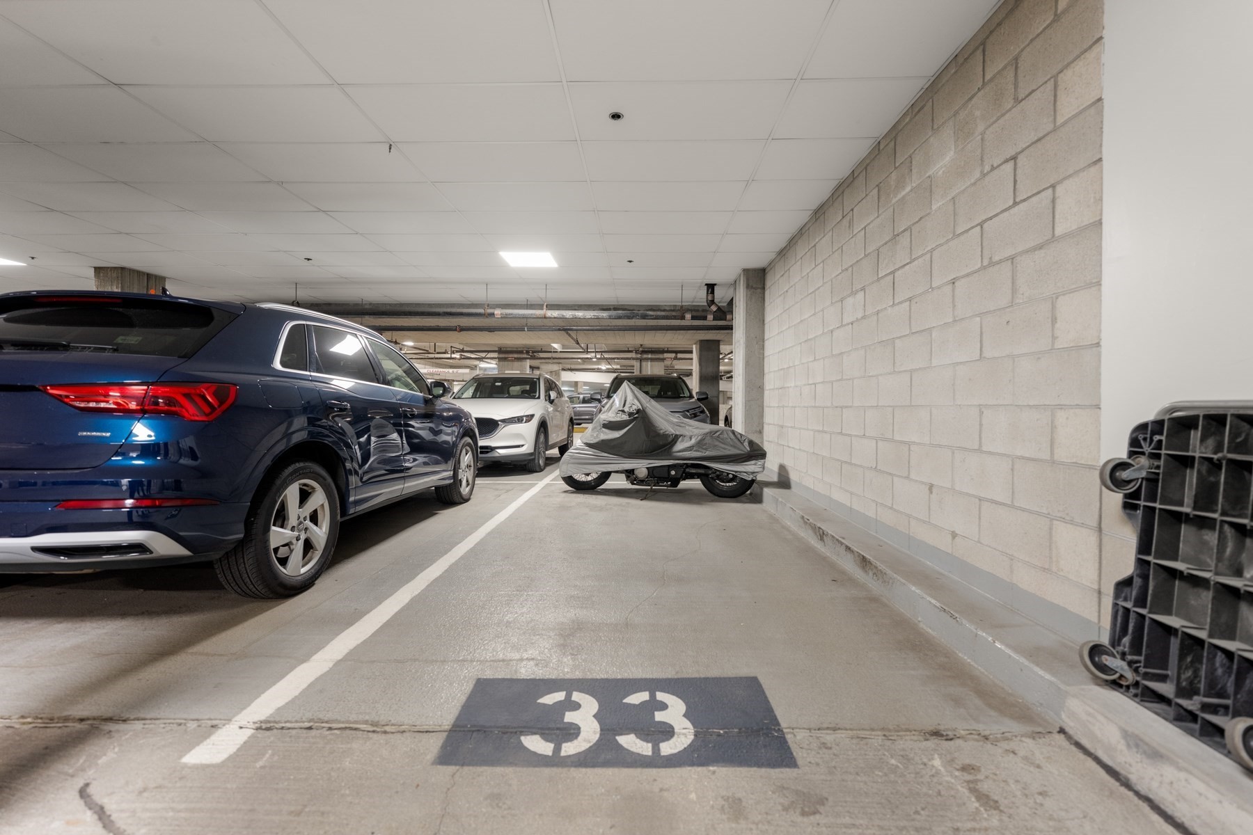 Indoor garage parking space 33 beside parked cars and a covered motorcycle.