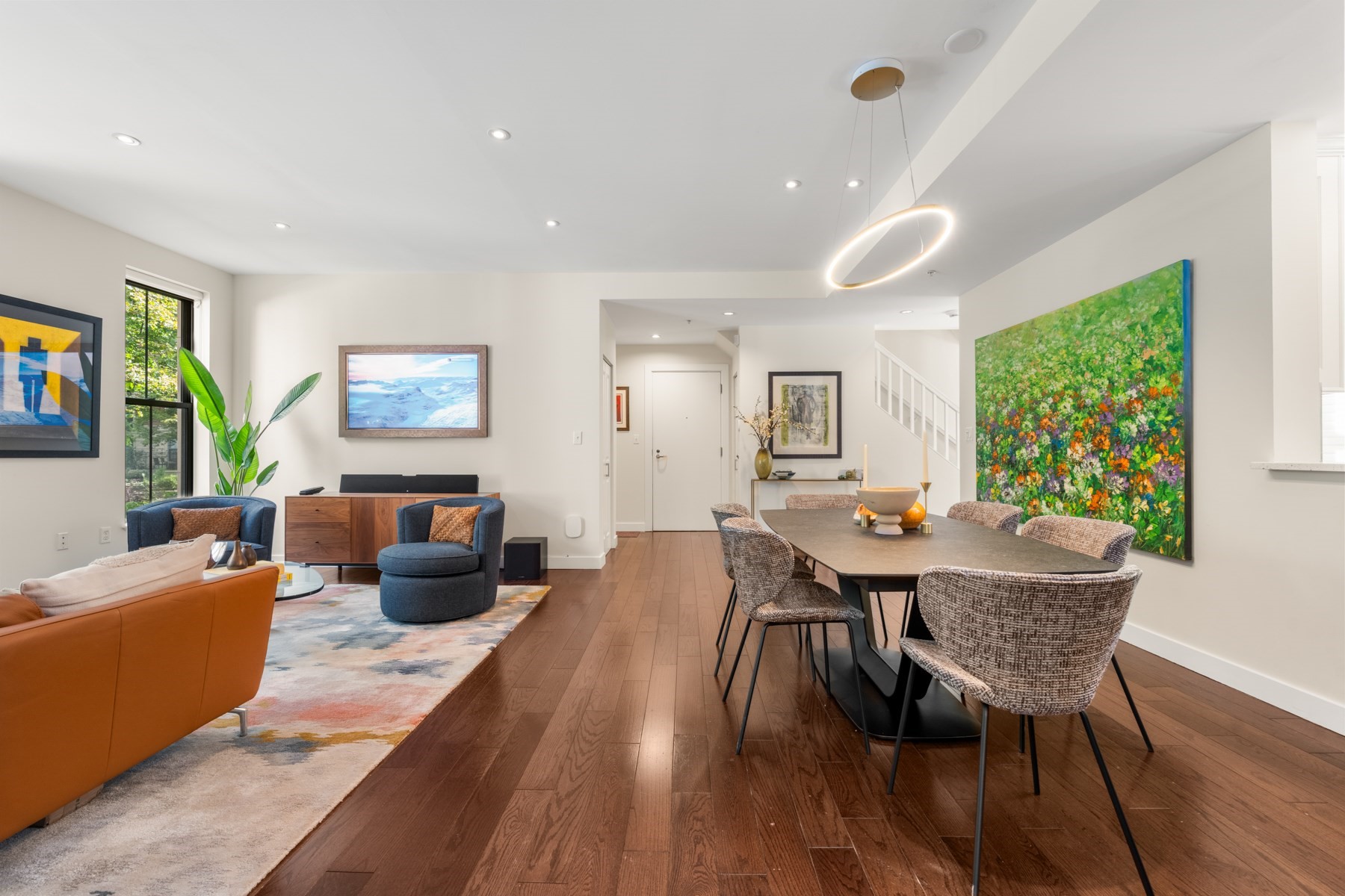 Open-plan living and dining room with hardwood floors, colorful artwork, and a large dining table.