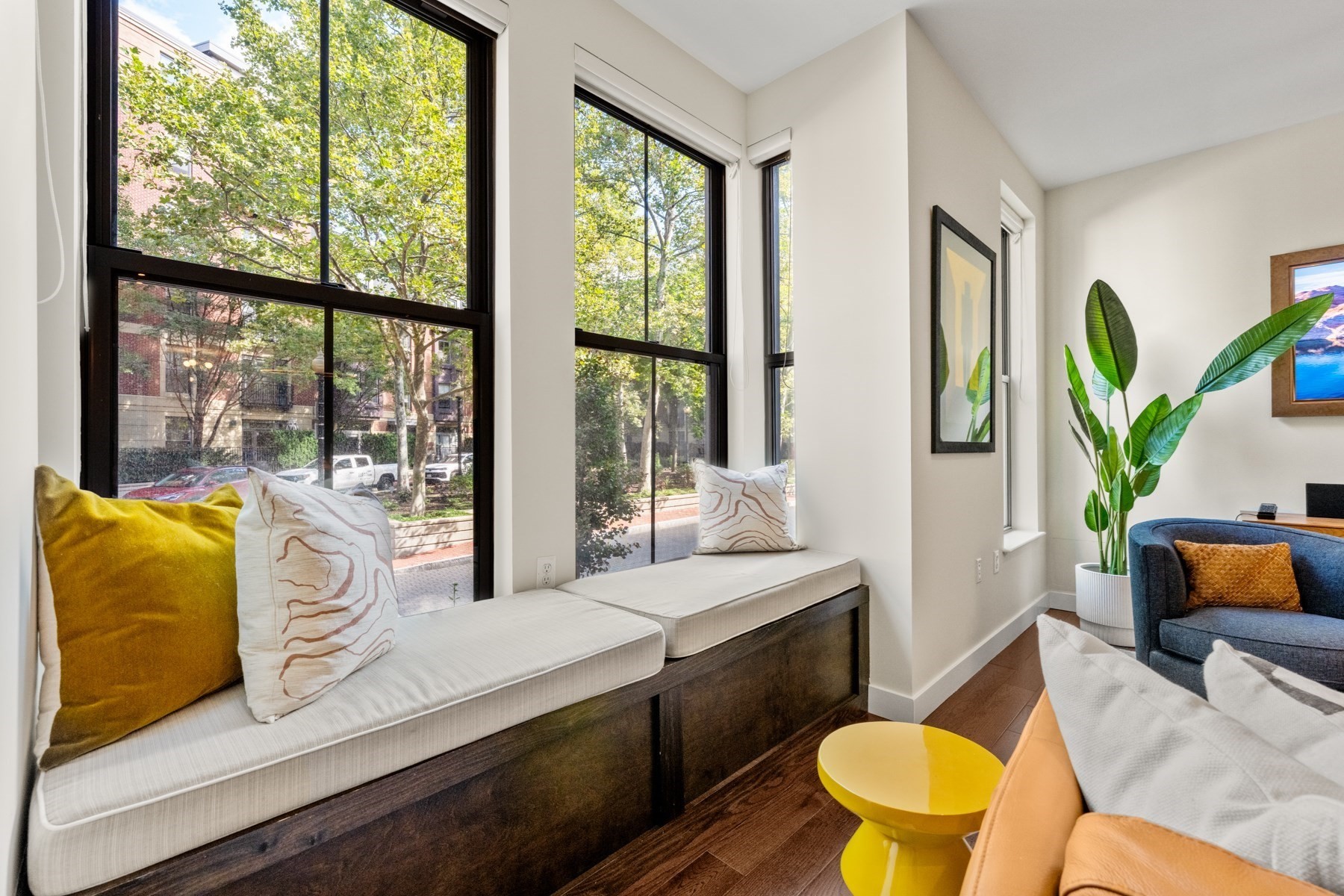 Living room with a cushioned window bench, tall street-facing windows, and a bright yellow coffee table.