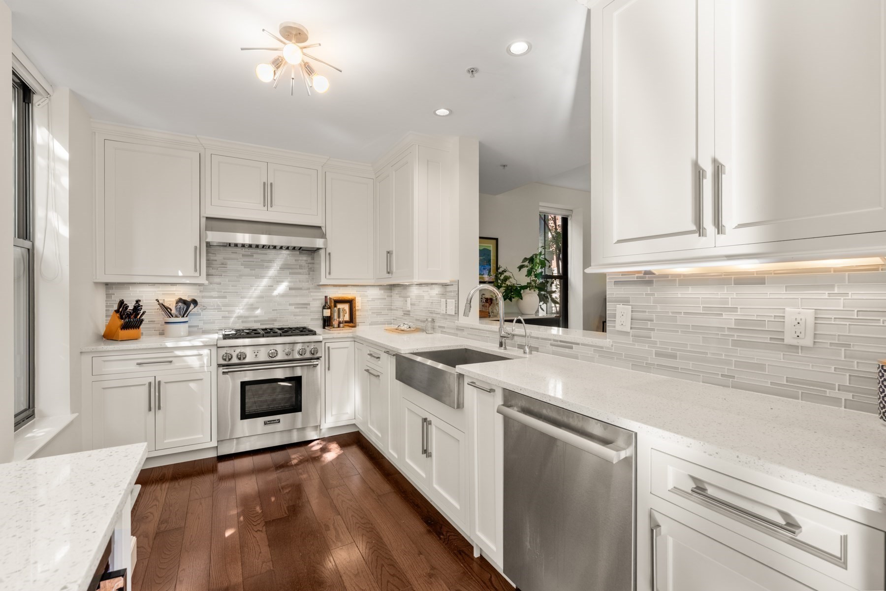 Bright white kitchen with stainless steel appliances, gray tile backsplash, and dark hardwood floors.
