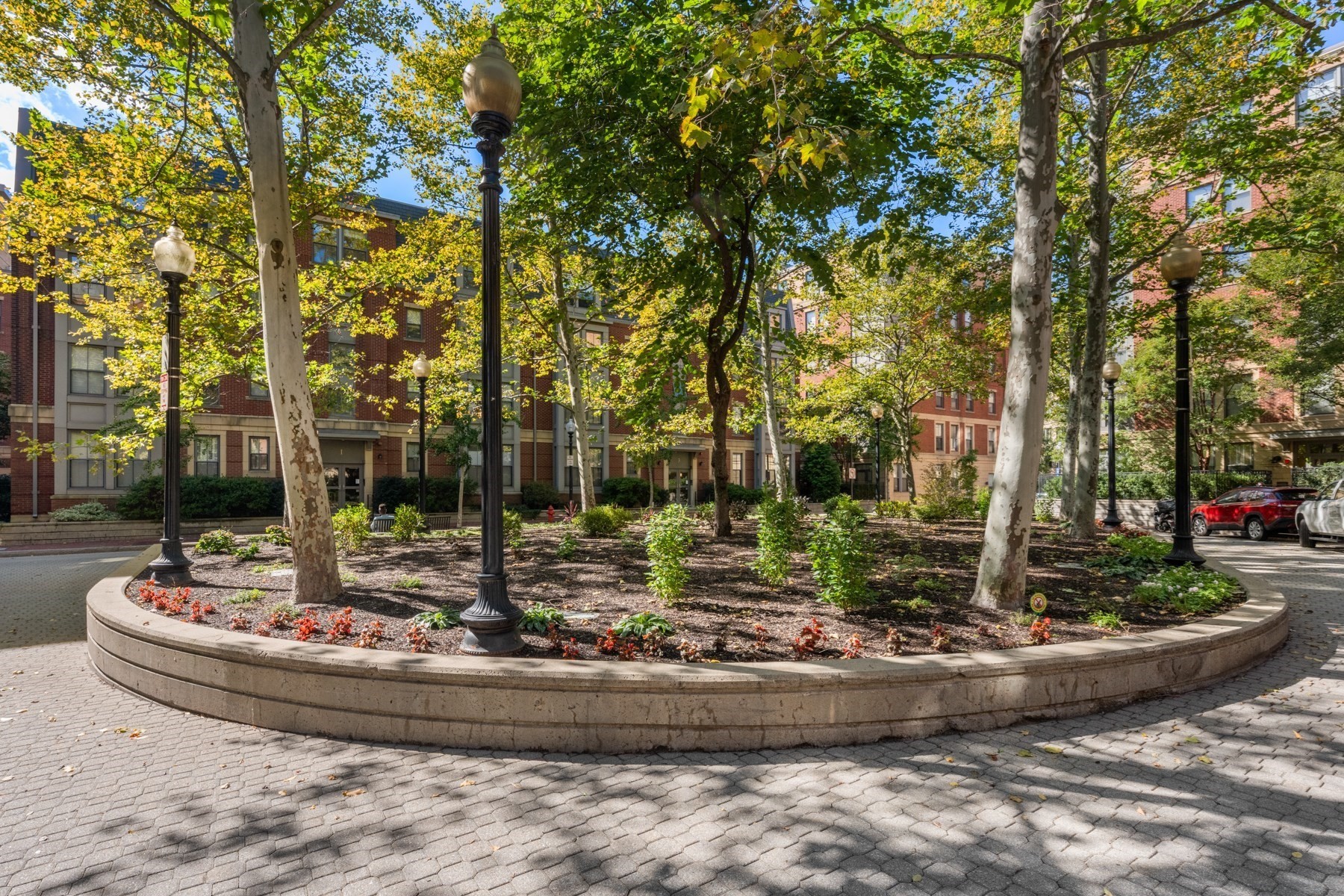 Apartment courtyard with mature trees, flower beds, and globe-topped lampposts.