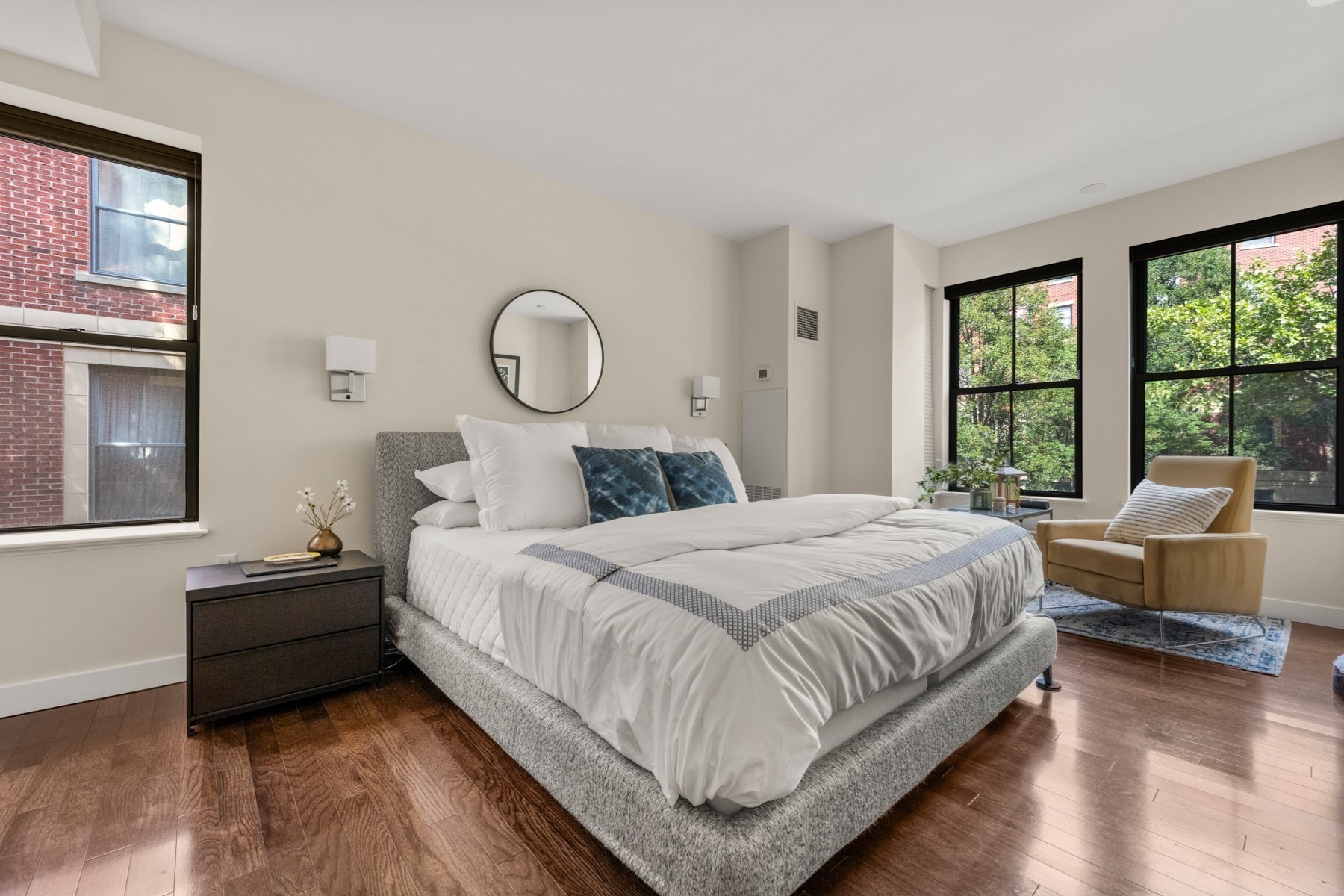 Bedroom with a large white bed, blue accent pillows, tall windows, and a tan armchair.