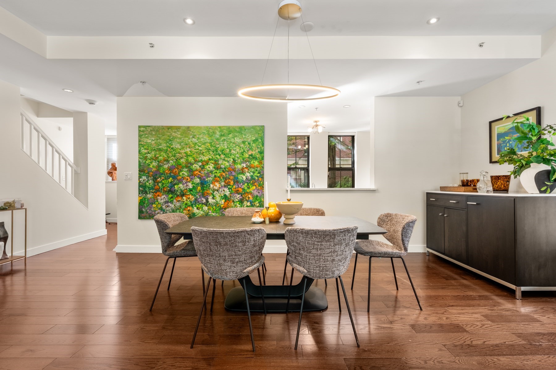 Furnished dining room with hardwood floors, a large floral painting, and a circular pendant light.