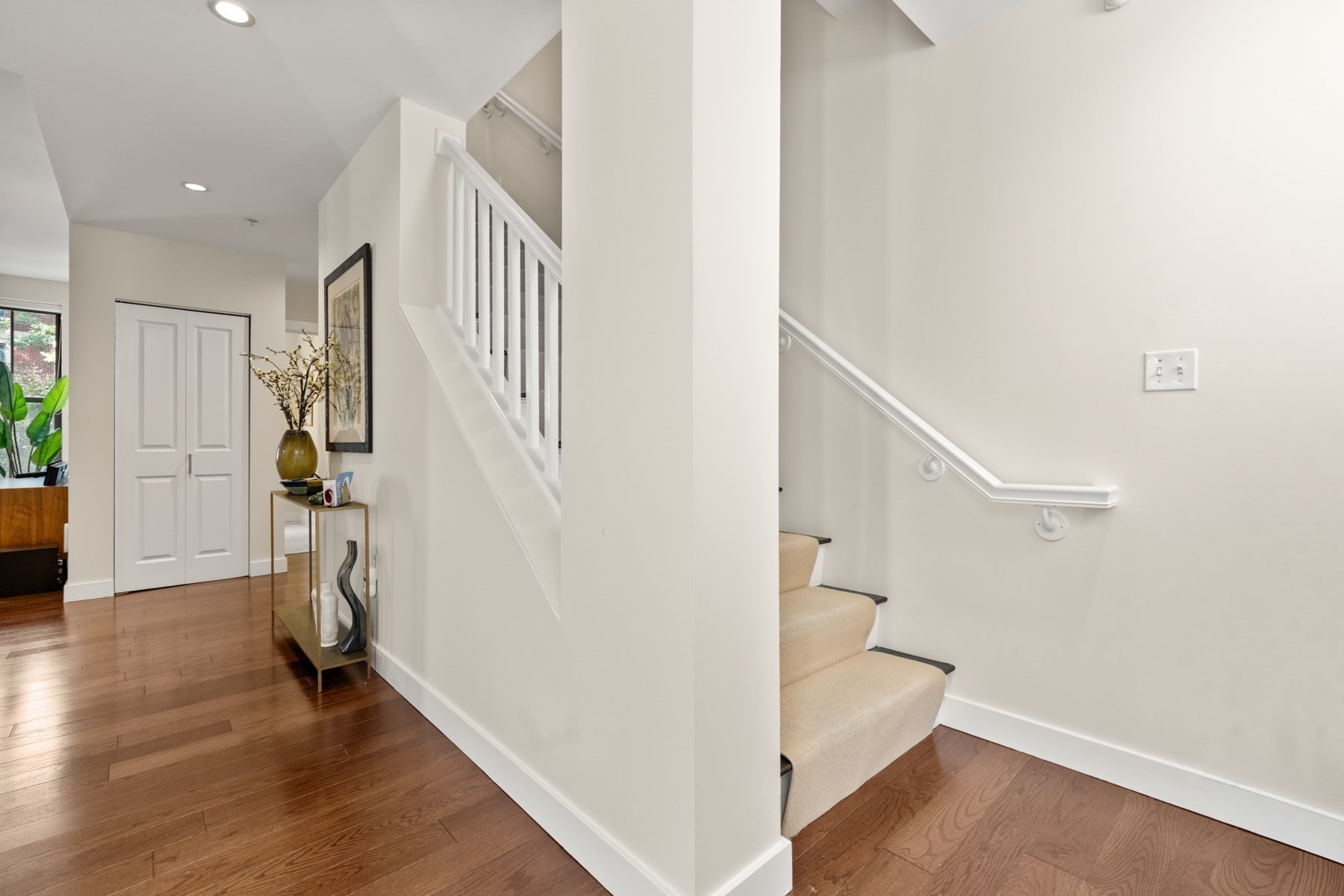 Entry hall with hardwood floors, a carpeted staircase, and a decorated console table.