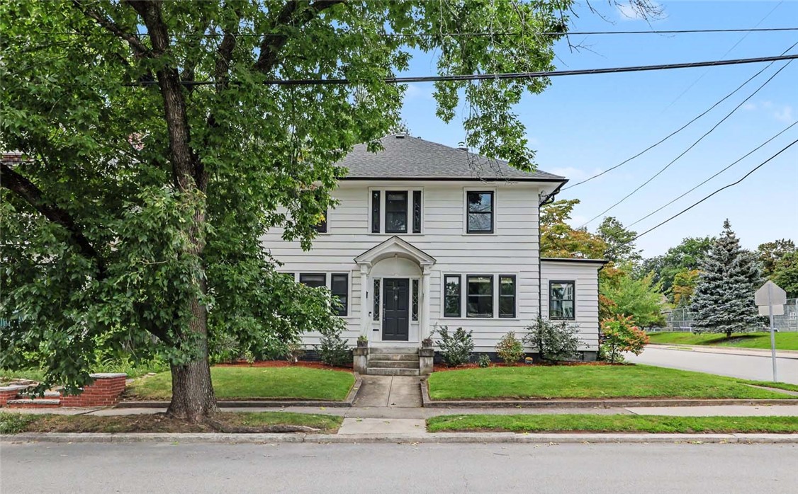 White two-story house with a covered entry, dark windows, and a large tree in front.