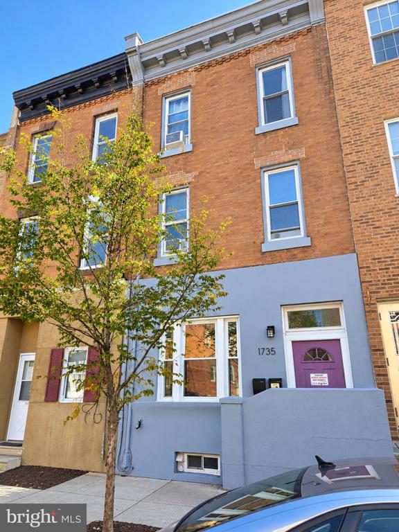 Brick rowhouse with a blue-gray lower facade, purple entry door, and a tree in front.