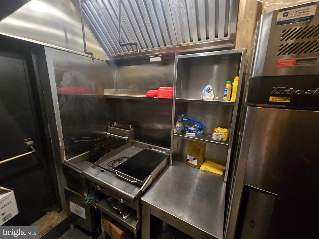 Commercial kitchen with stainless-steel cooking equipment, an overhead exhaust hood, and open shelving.