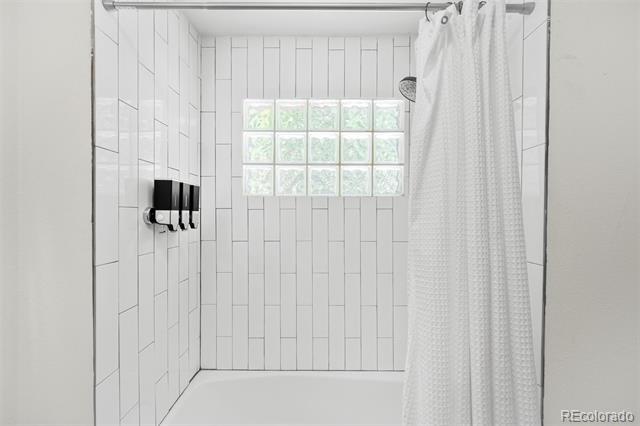 White-tiled shower with a glass-block window, black controls, and a white curtain.