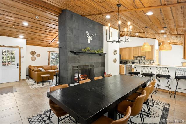 Open-plan dining area with a long black table, exposed wood ceiling, and stone fireplace.