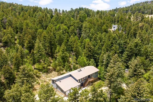 Aerial view of a long house nestled among dense evergreen trees on a wooded hillside.