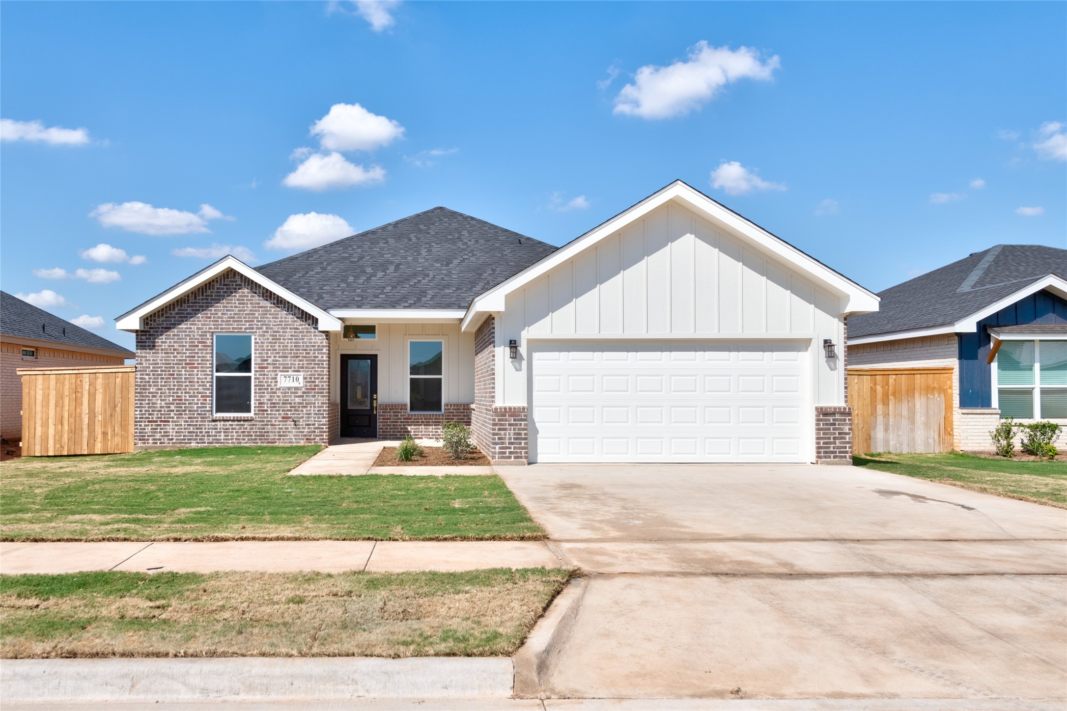 Single-story brick and white-sided house with a two-car garage, broad driveway, and front lawn.