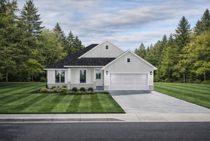 White house with a two-car garage, striped lawn, and wooded surroundings.