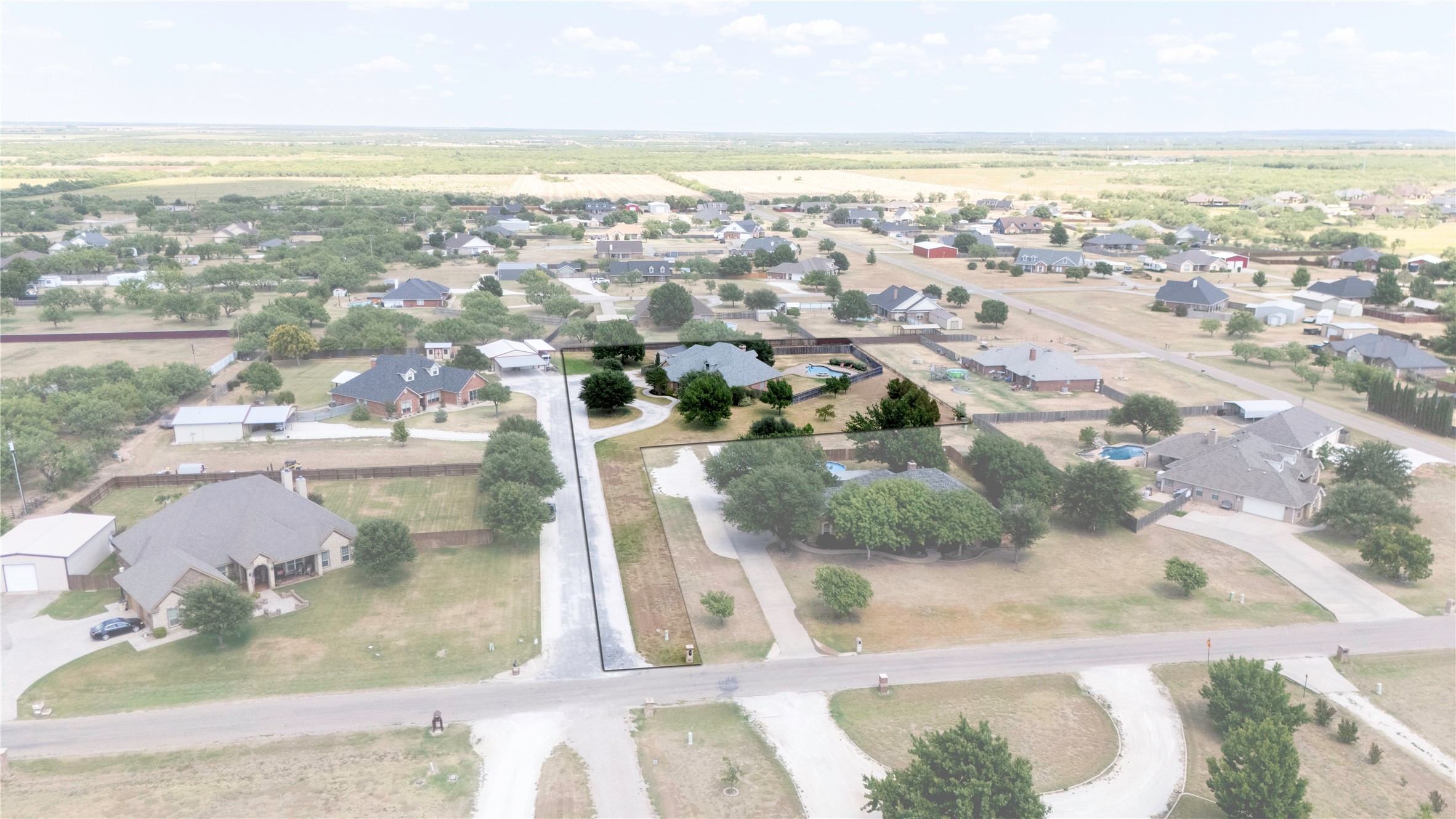 Aerial view of a residential property with a long driveway, mature trees, and a backyard pool.