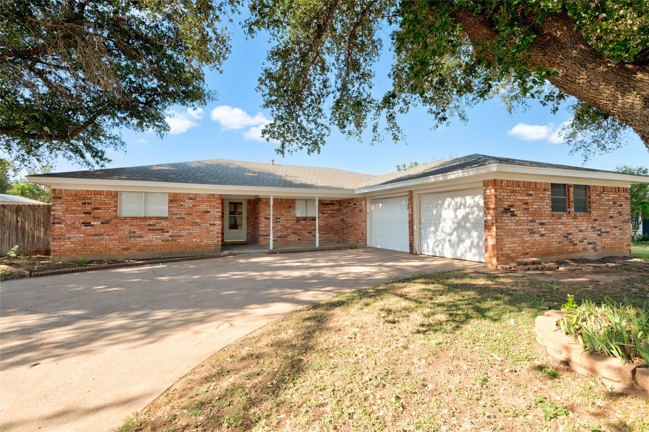 Single-story brick house with an attached garage, wide driveway, and mature shade trees.