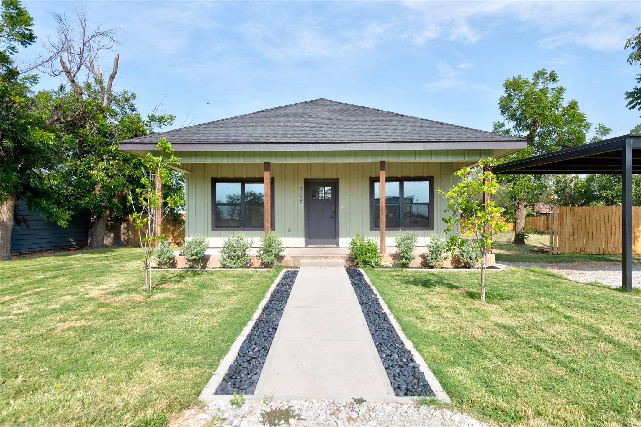 Single-story pale green house with a covered porch, landscaped lawn, and walkway to the entrance.