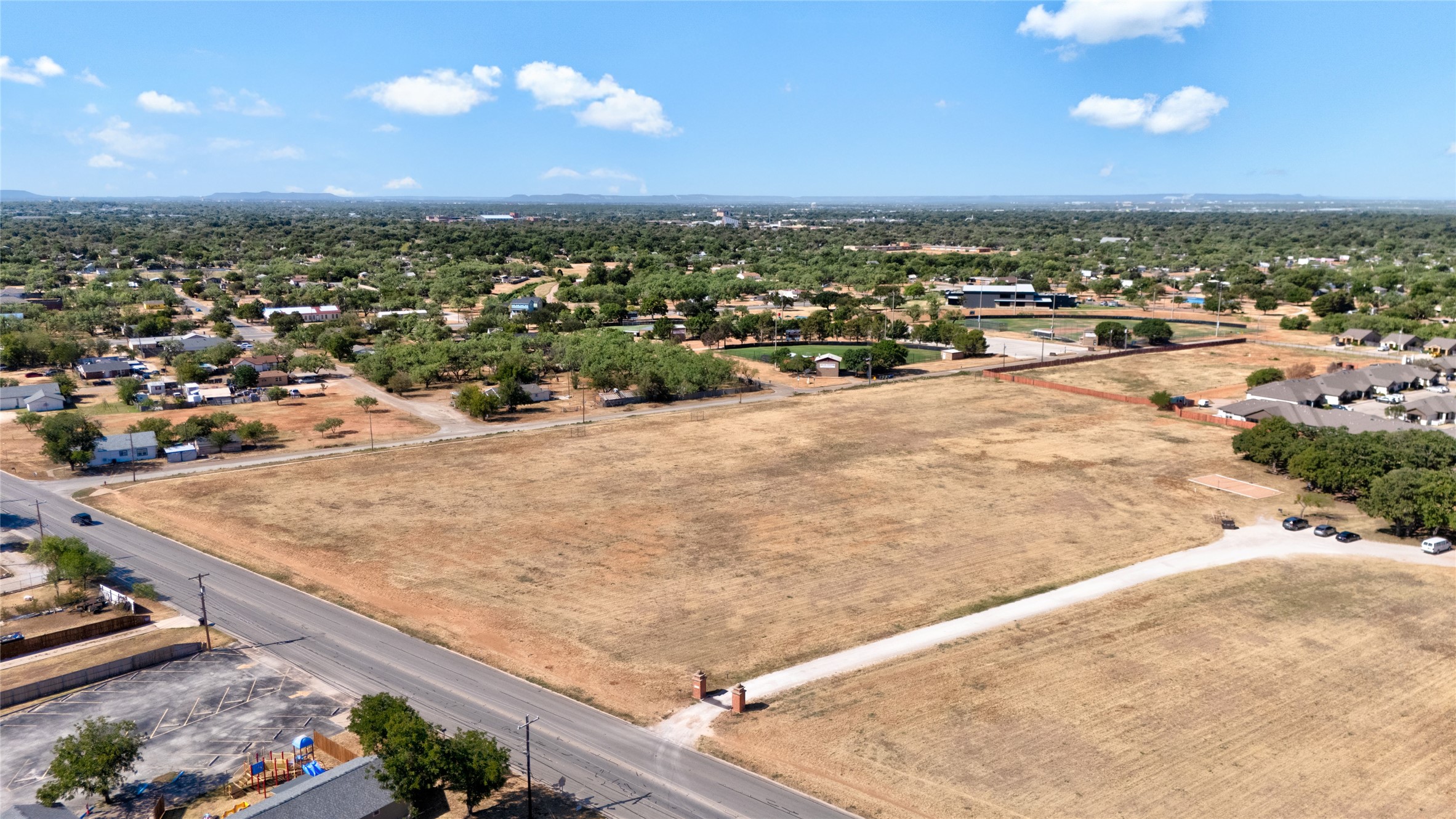 Aerial view of a large vacant, dry lot beside a road and nearby homes.