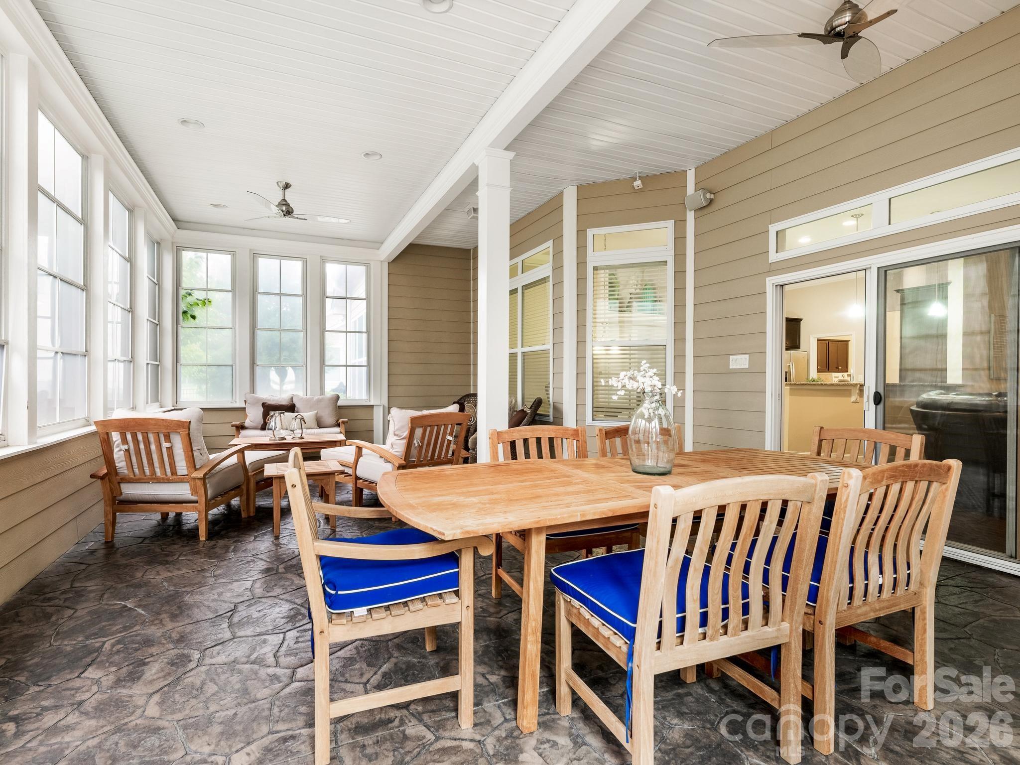 Covered porch with a wooden dining set, blue chair cushions, stone-pattern flooring, and a bright sitting area.