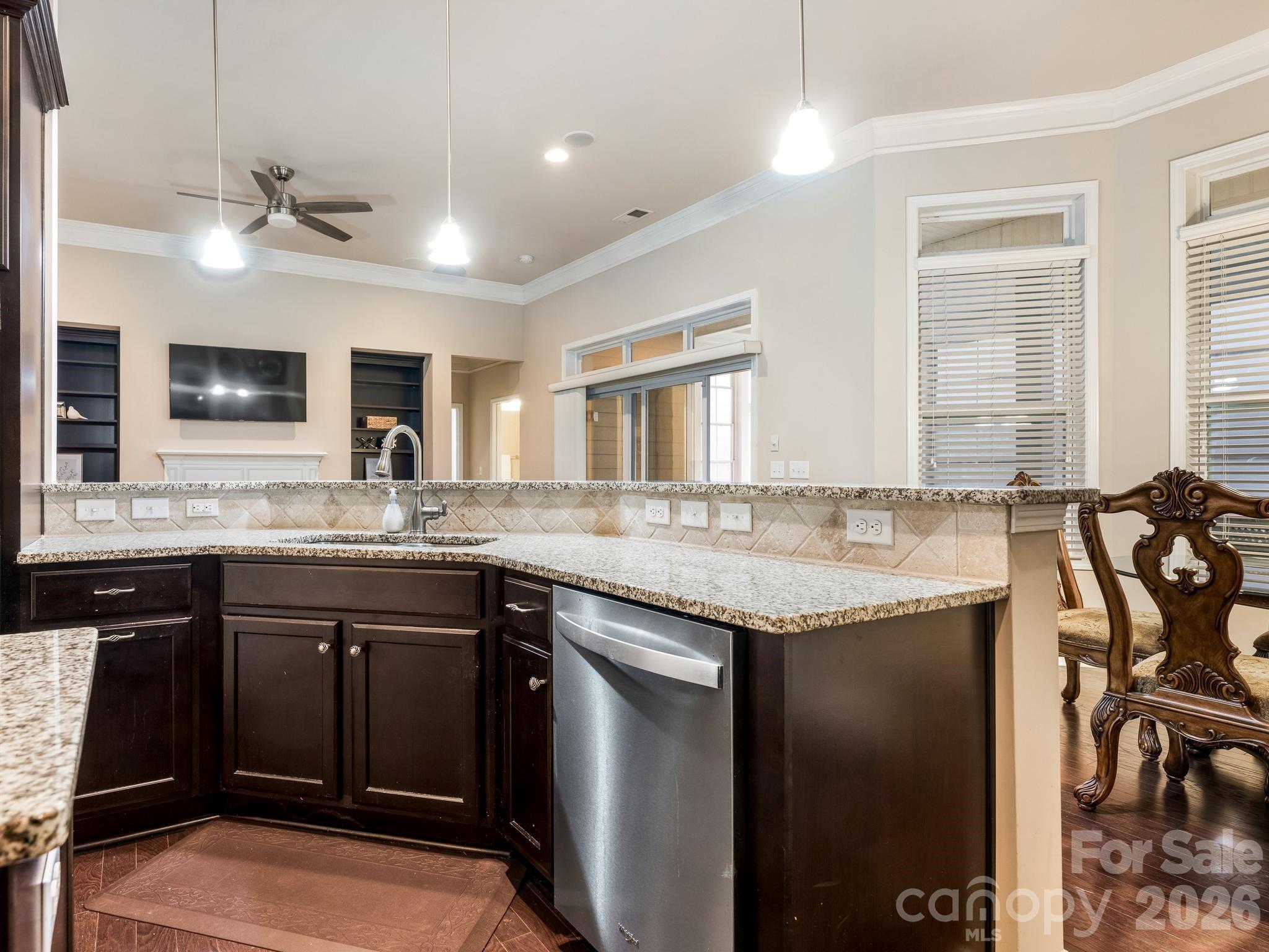 Kitchen with dark wood cabinets and granite counters, opening to a living area with a fireplace and television.