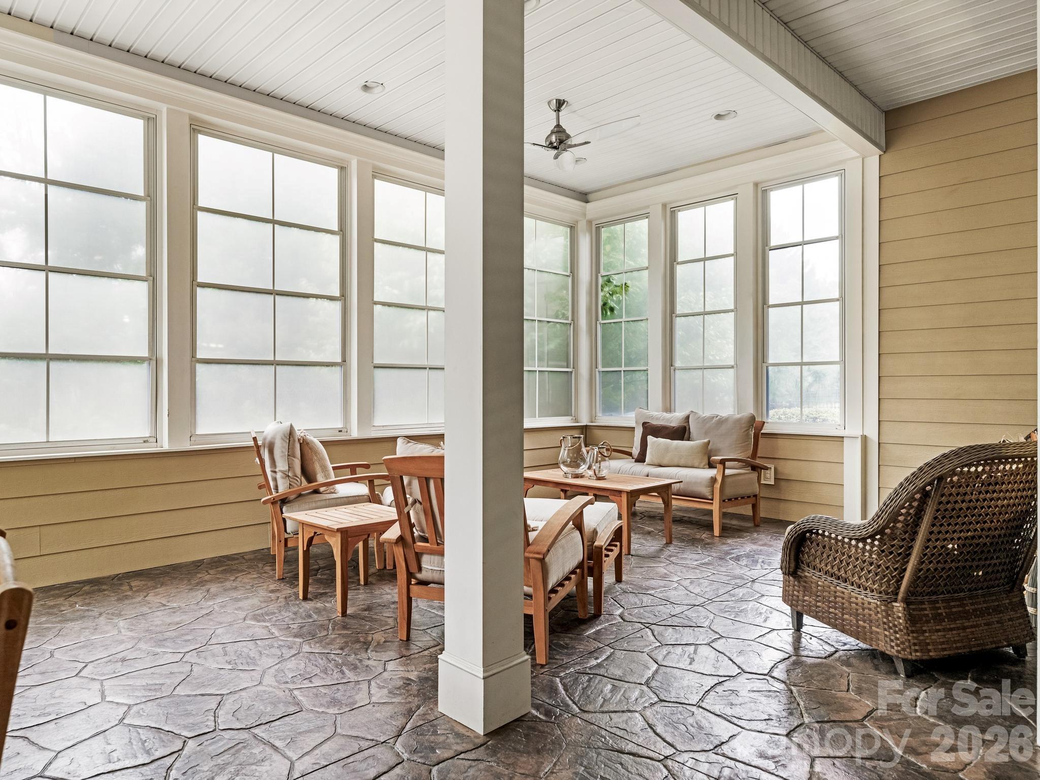 Furnished sunroom with expansive windows, flagstone flooring, wood seating, and a wicker chair.