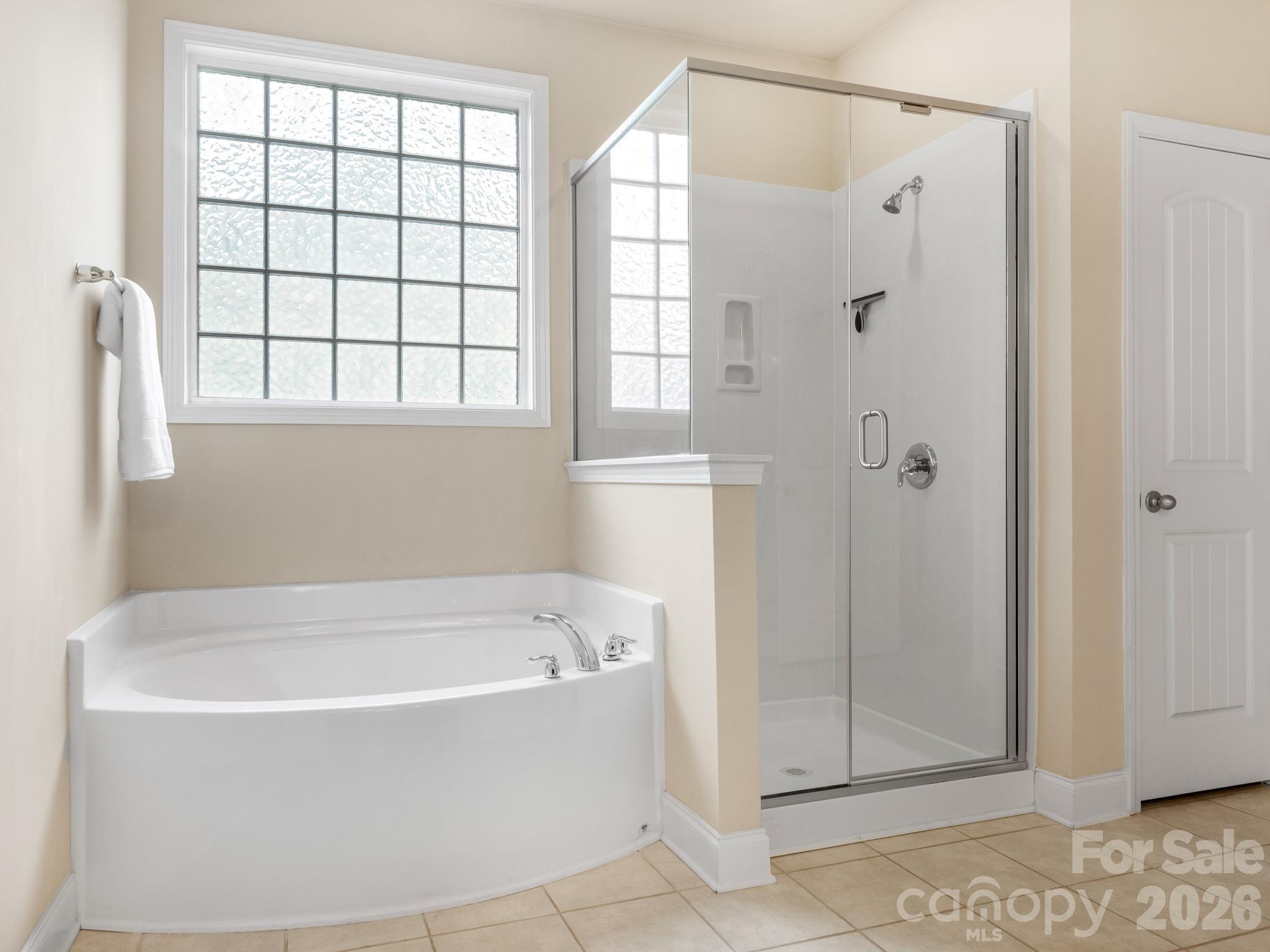 Bathroom with a corner soaking tub, glass-enclosed shower, and large frosted window.