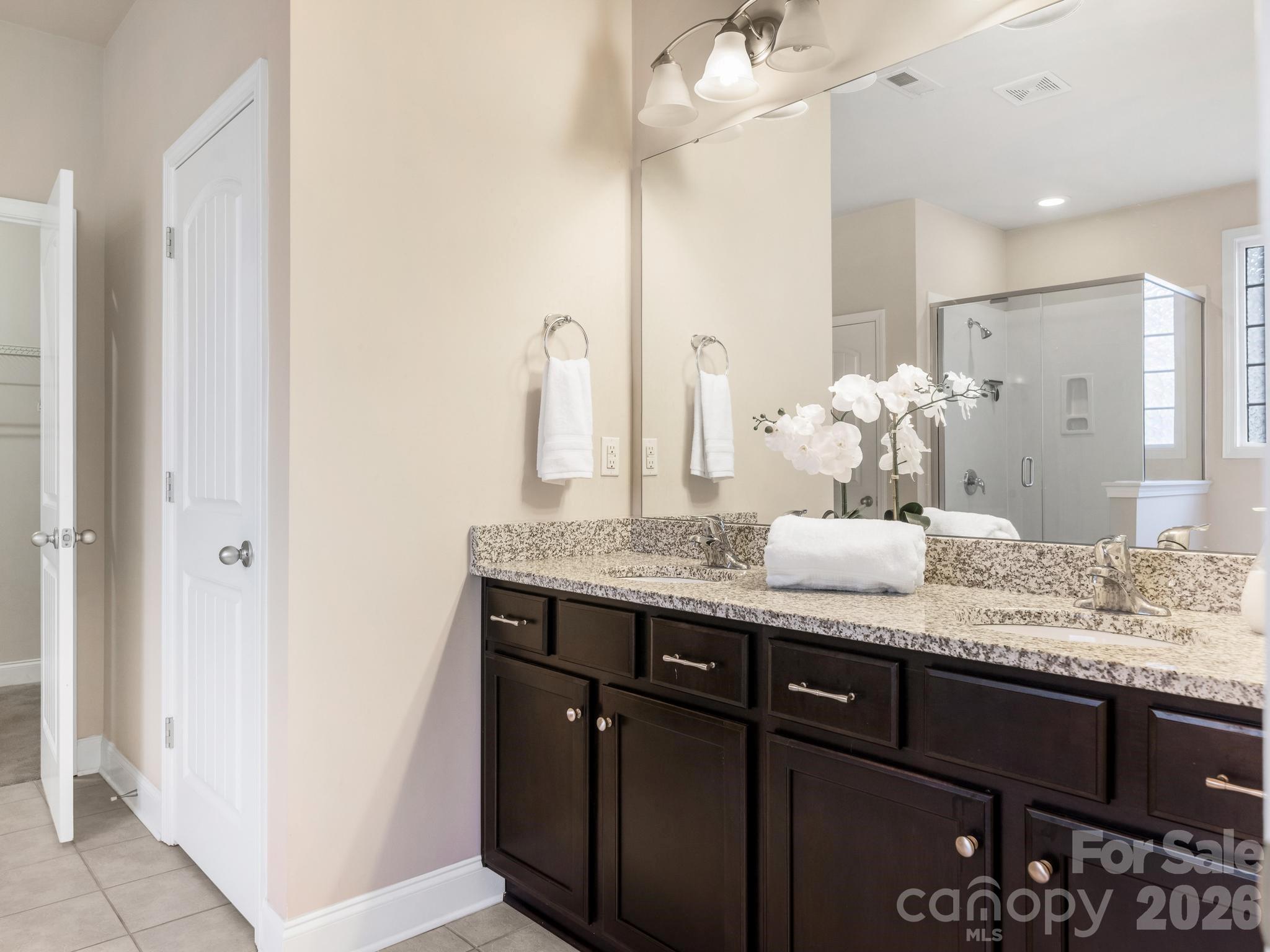 Bathroom with a dark wood double vanity, granite counter, large mirror, and glass shower.