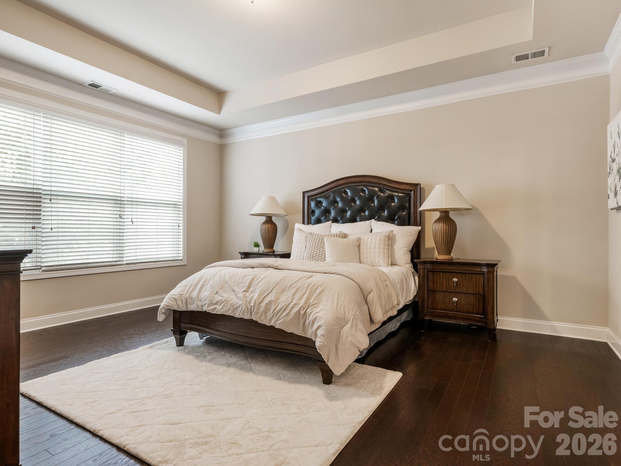 Furnished bedroom with a dark tufted headboard, white bedding, matching nightstands, and a large window.