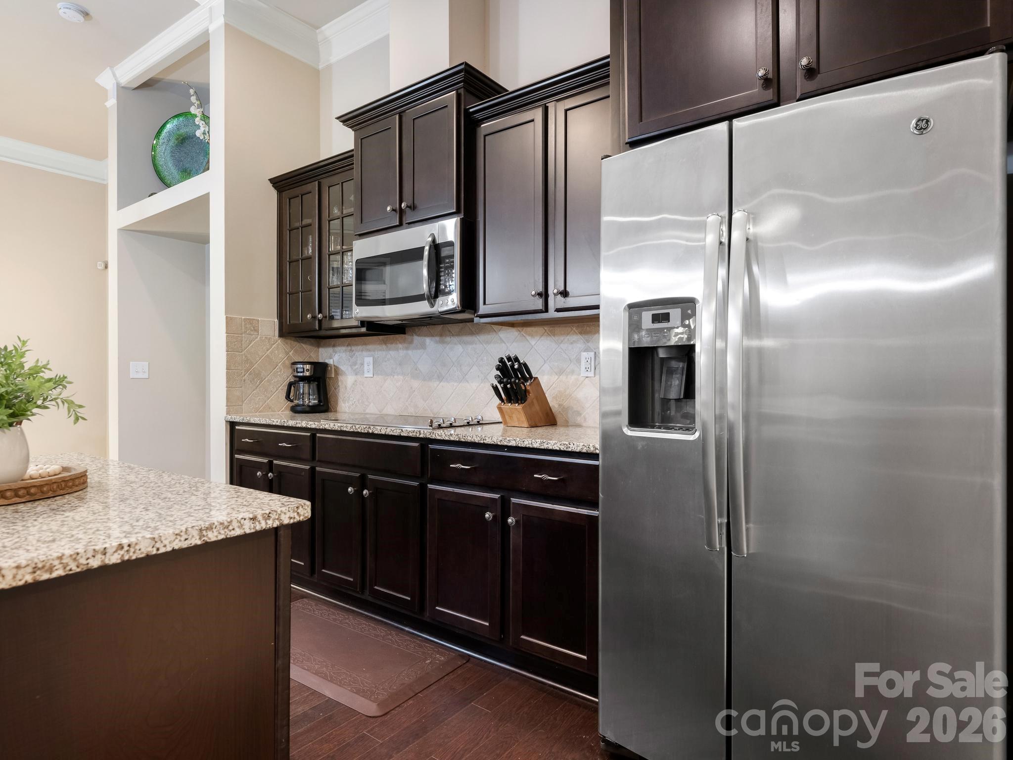 Kitchen with dark wood cabinets, granite counters, and a stainless steel refrigerator.