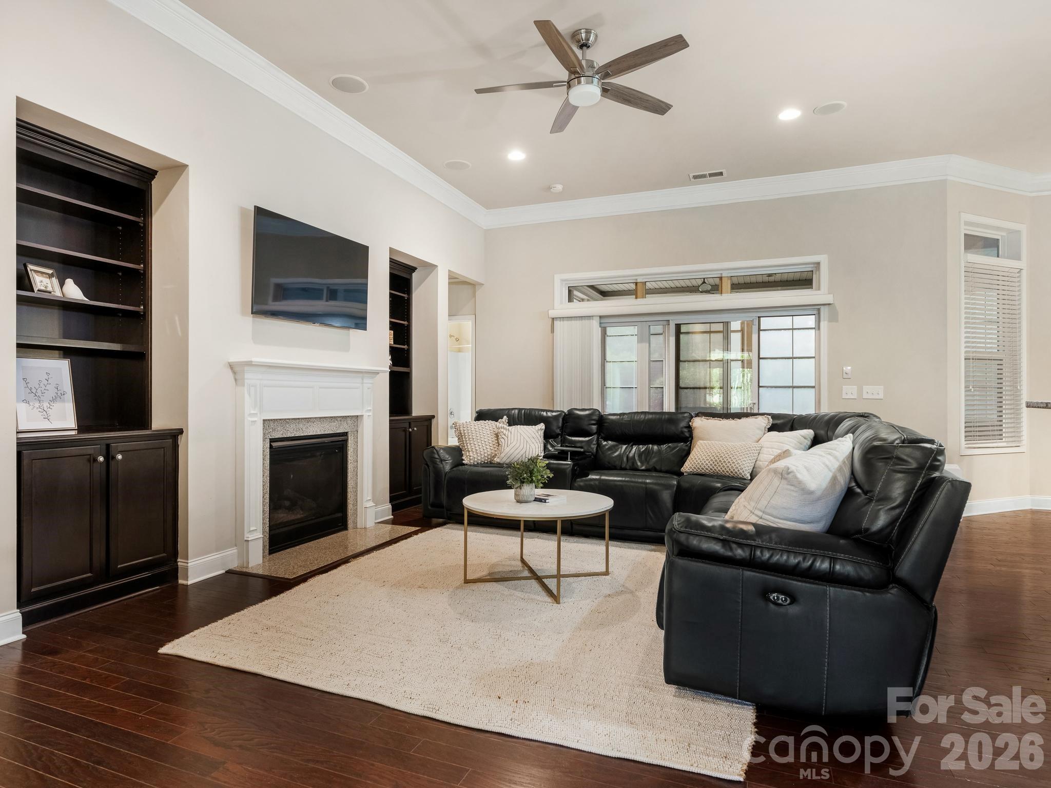 Living room with a black leather sectional, built-in shelves, fireplace, and glass doors to a covered patio.