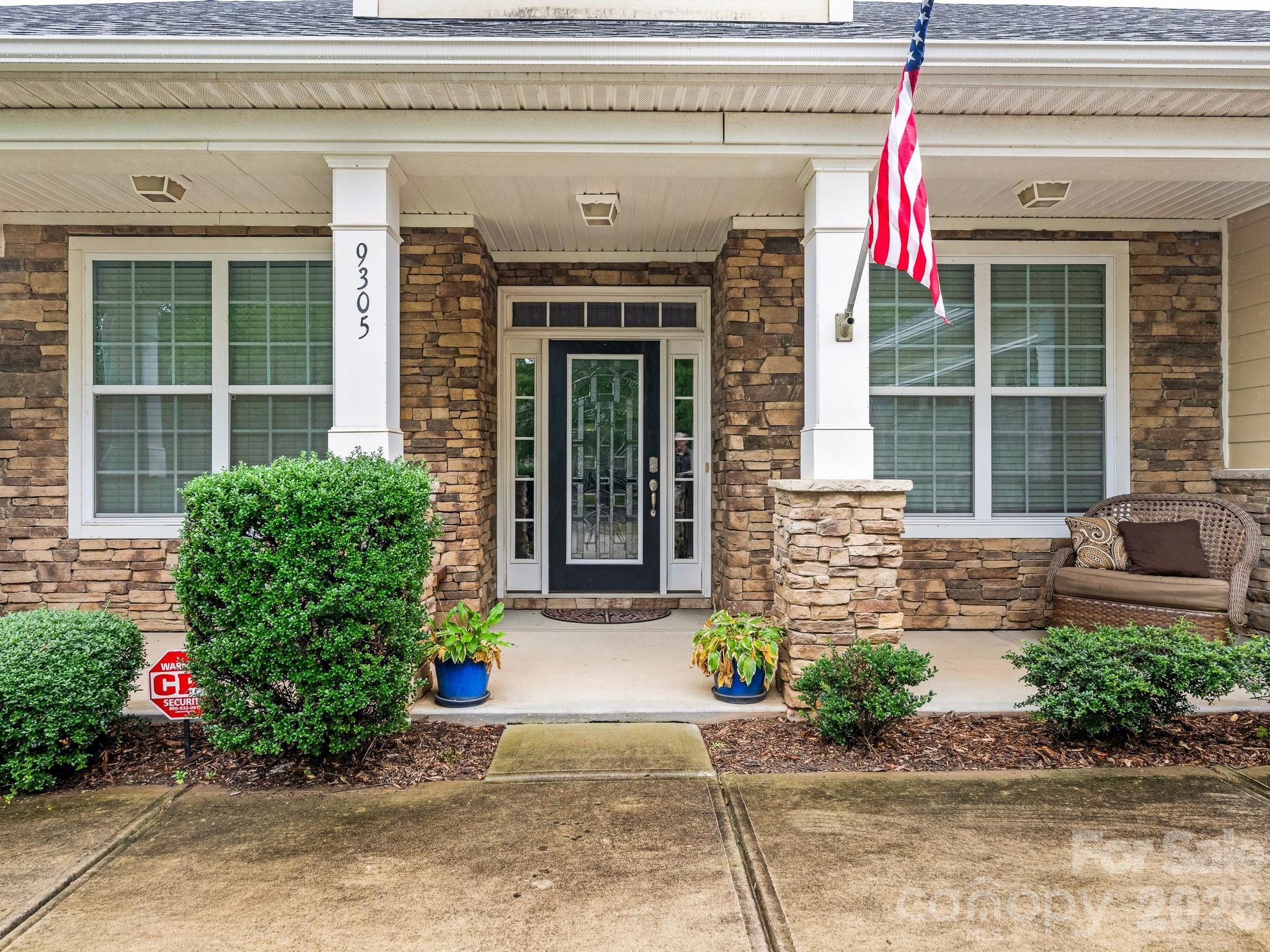 Stone-front home entrance with a covered porch, American flag, and 9305 displayed on a column.