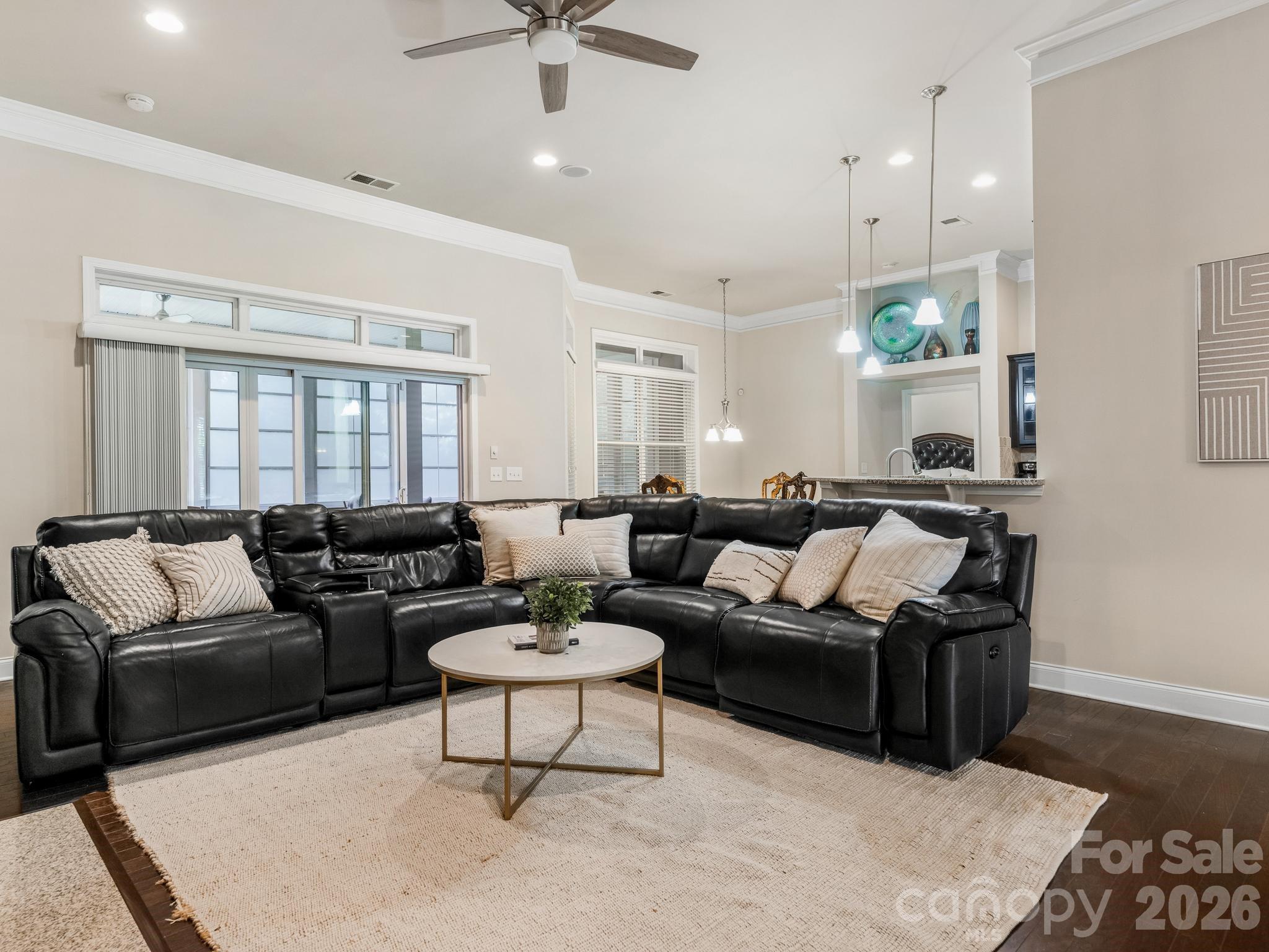 Living room with a black leather sectional, round coffee table, and wide windows opening toward the kitchen.