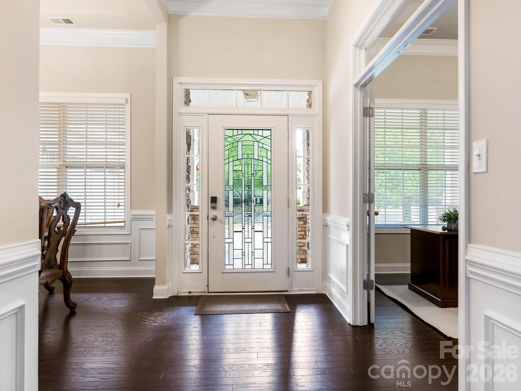 Front entry foyer with a decorative stained-glass door, dark hardwood floors, and white wainscoting.